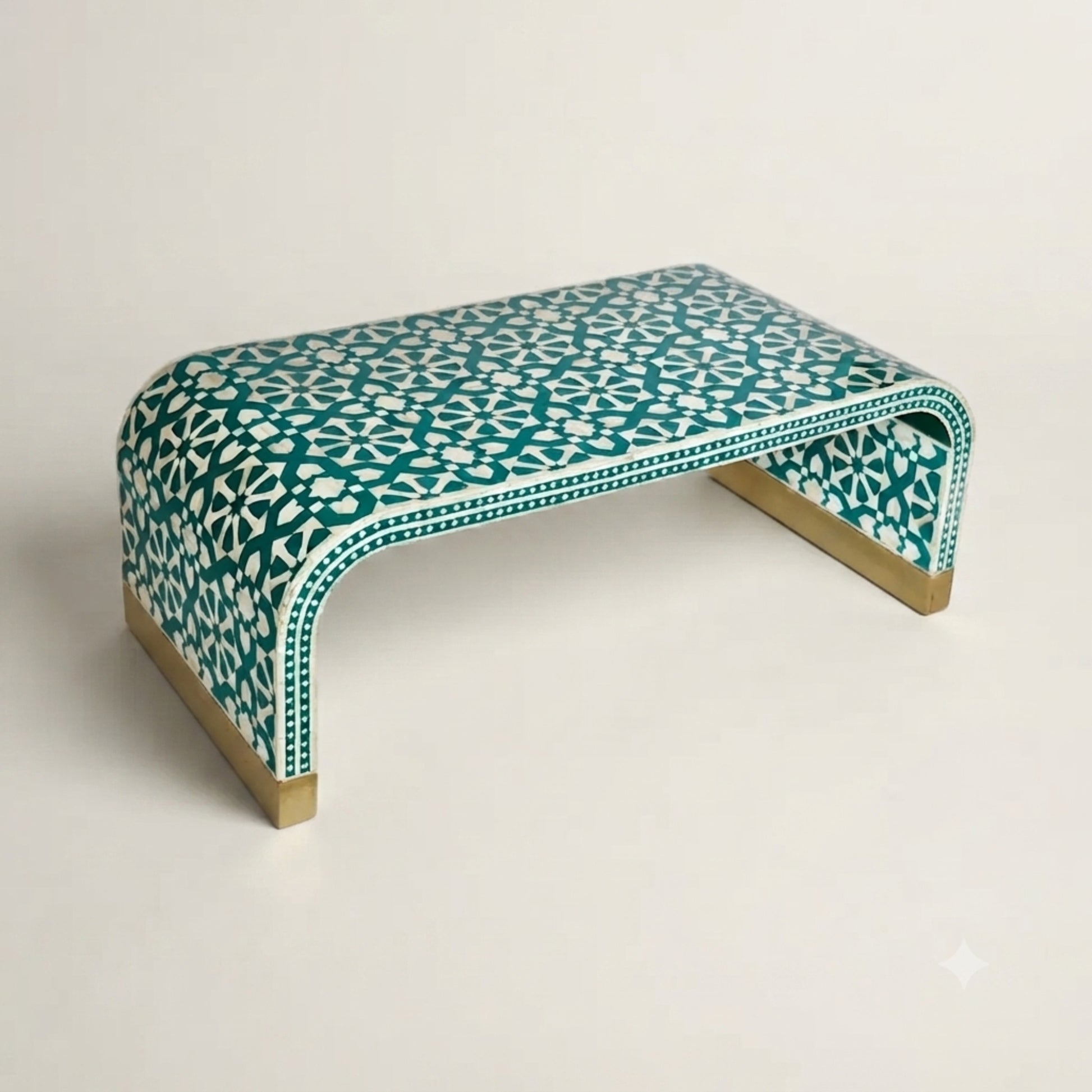 A modern curved bench with a teal and white geometric bone-inlay pattern and light wood legs, photographed on a clean off-white background.