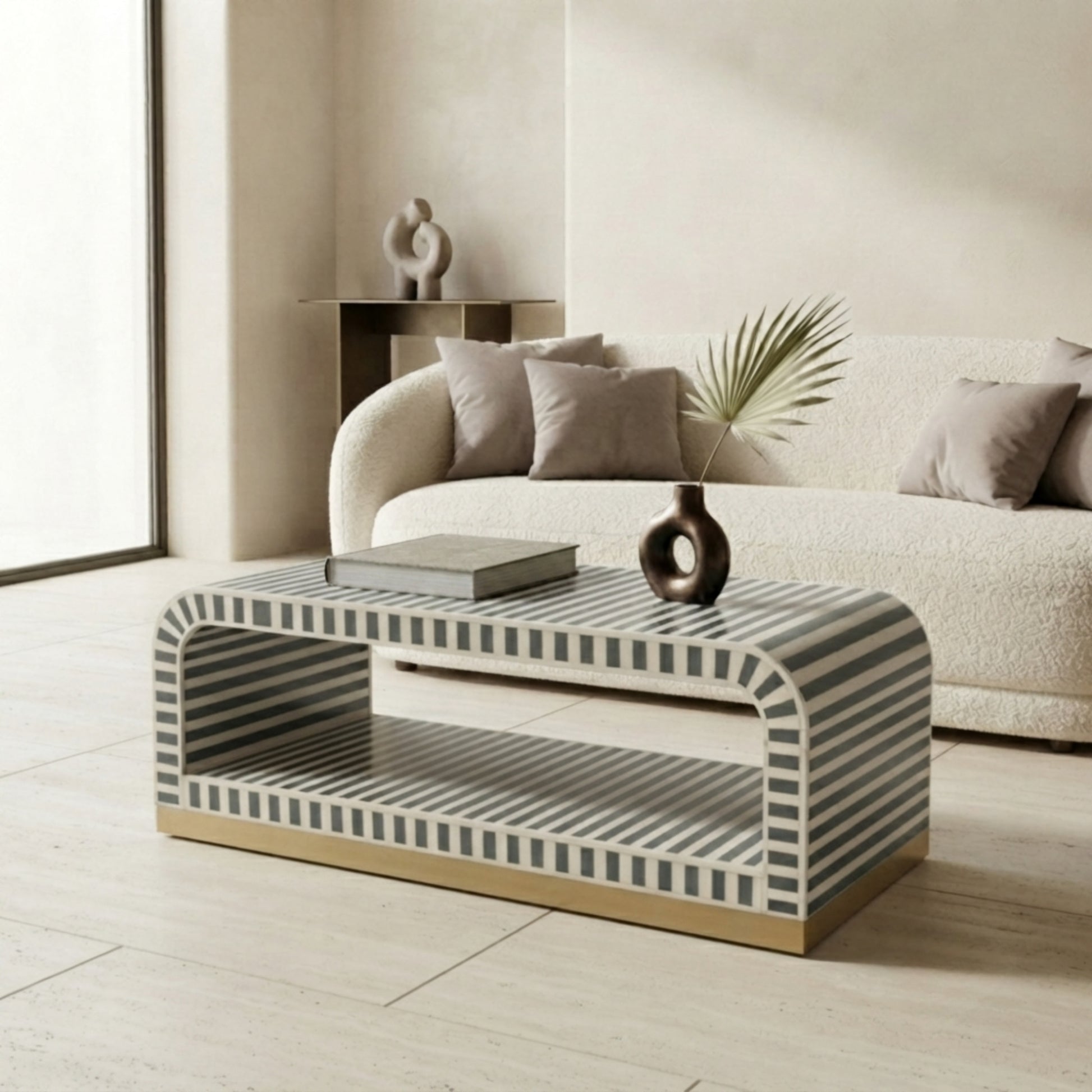 A modern rectangular coffee table with a curved top and open lower shelf, featuring a black and white striped pattern and a gold-toned base, styled in a contemporary living room setting.
