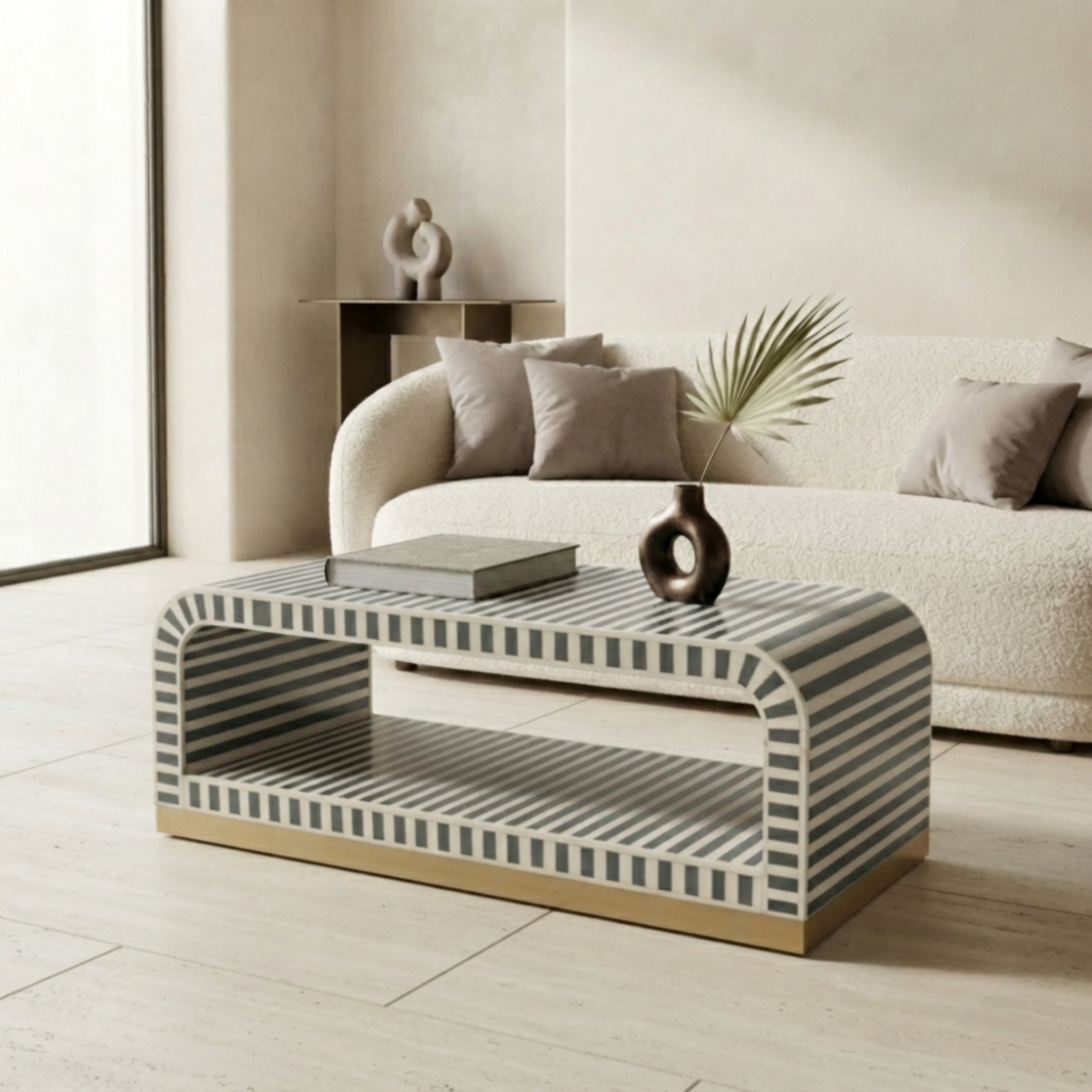 A modern rectangular coffee table with a curved top and open lower shelf, featuring a black and white striped pattern and a gold-toned base, styled in a contemporary living room setting.