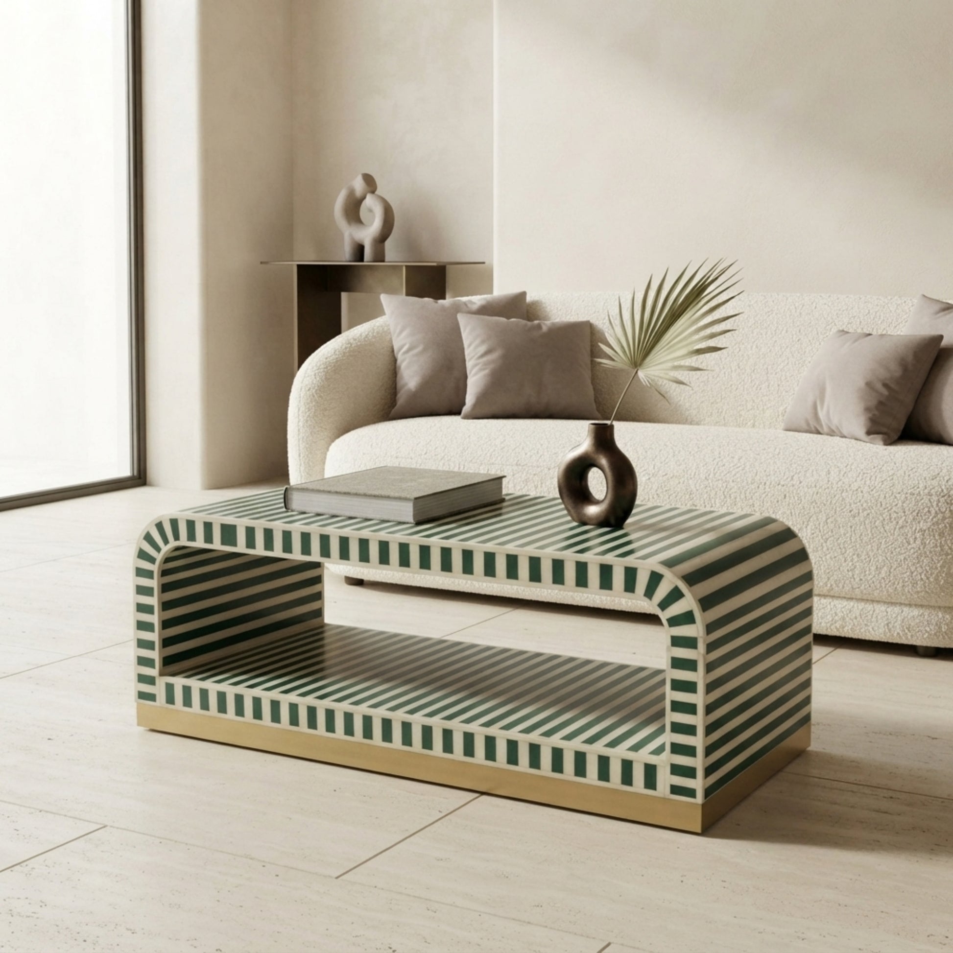 A modern rectangular coffee table with a green and white striped pattern and a gold metal base, styled in a minimalist living room next to a cream bouclé sofa.