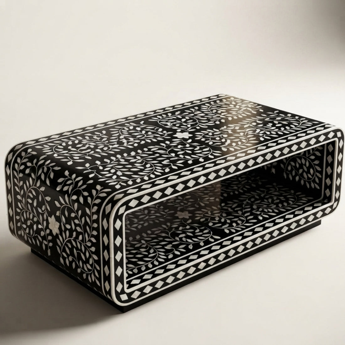 A modern rectangular coffee table with a glossy black and white geometric patterned bone-inlay frame, set in a minimalist living room with a white sofa and neutral decor.