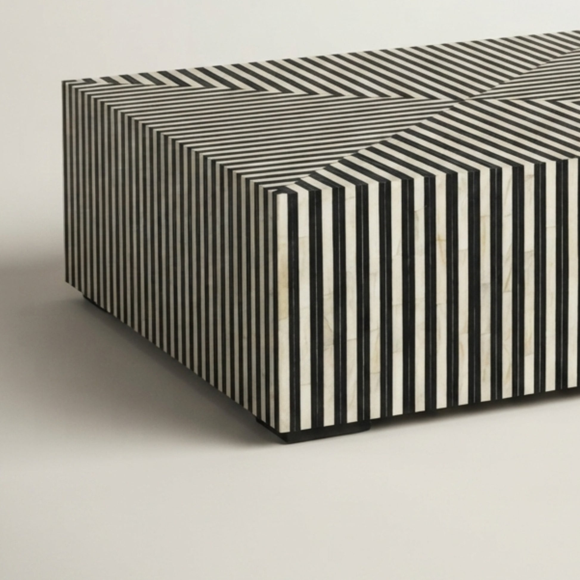 A rectangular ottoman or bench with a geometric black and off-white striped bone-inwood pattern, shown on a neutral light gray background.