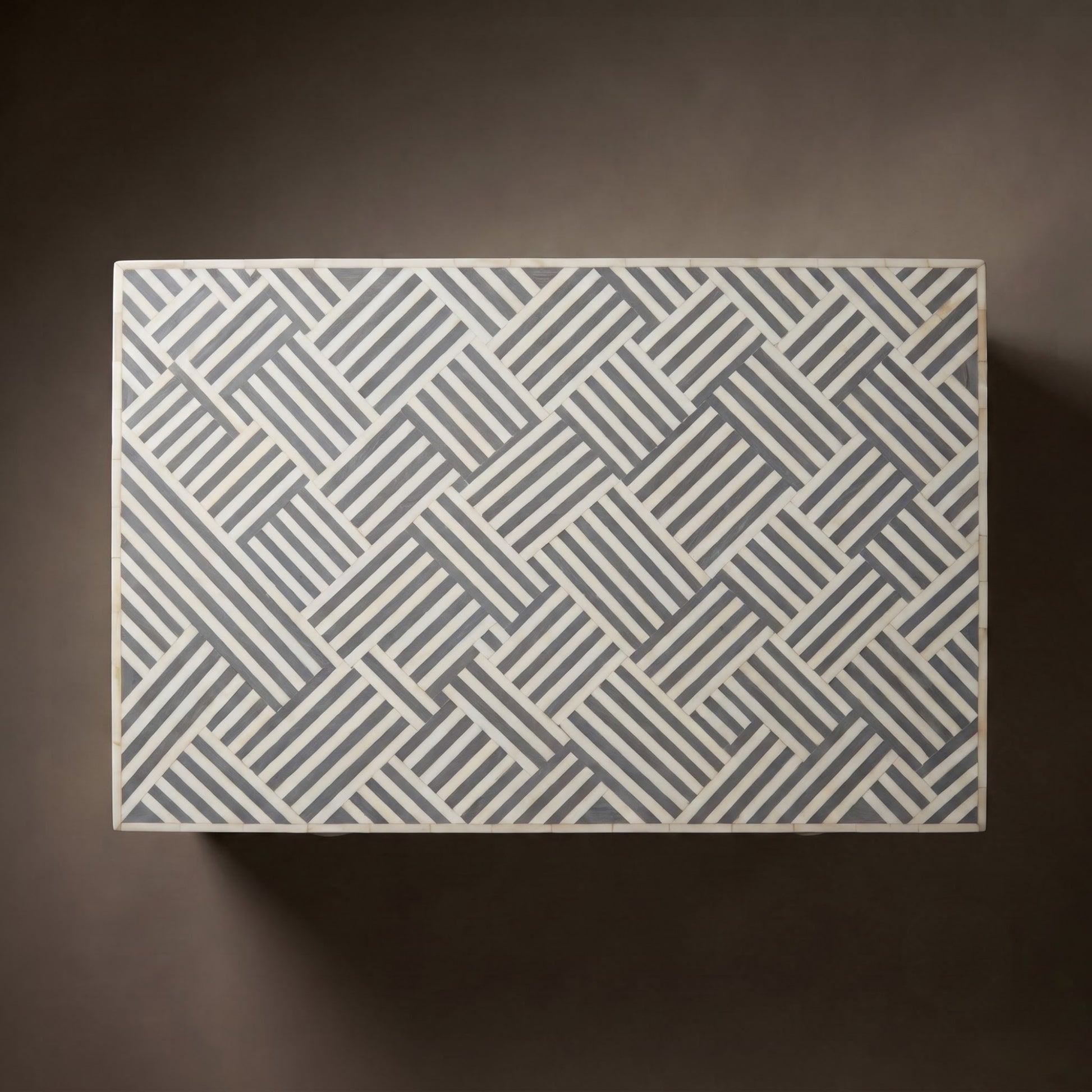 A rectangular box with a geometric basketweave pattern in gray and white, photographed from directly above against a dark brown background.