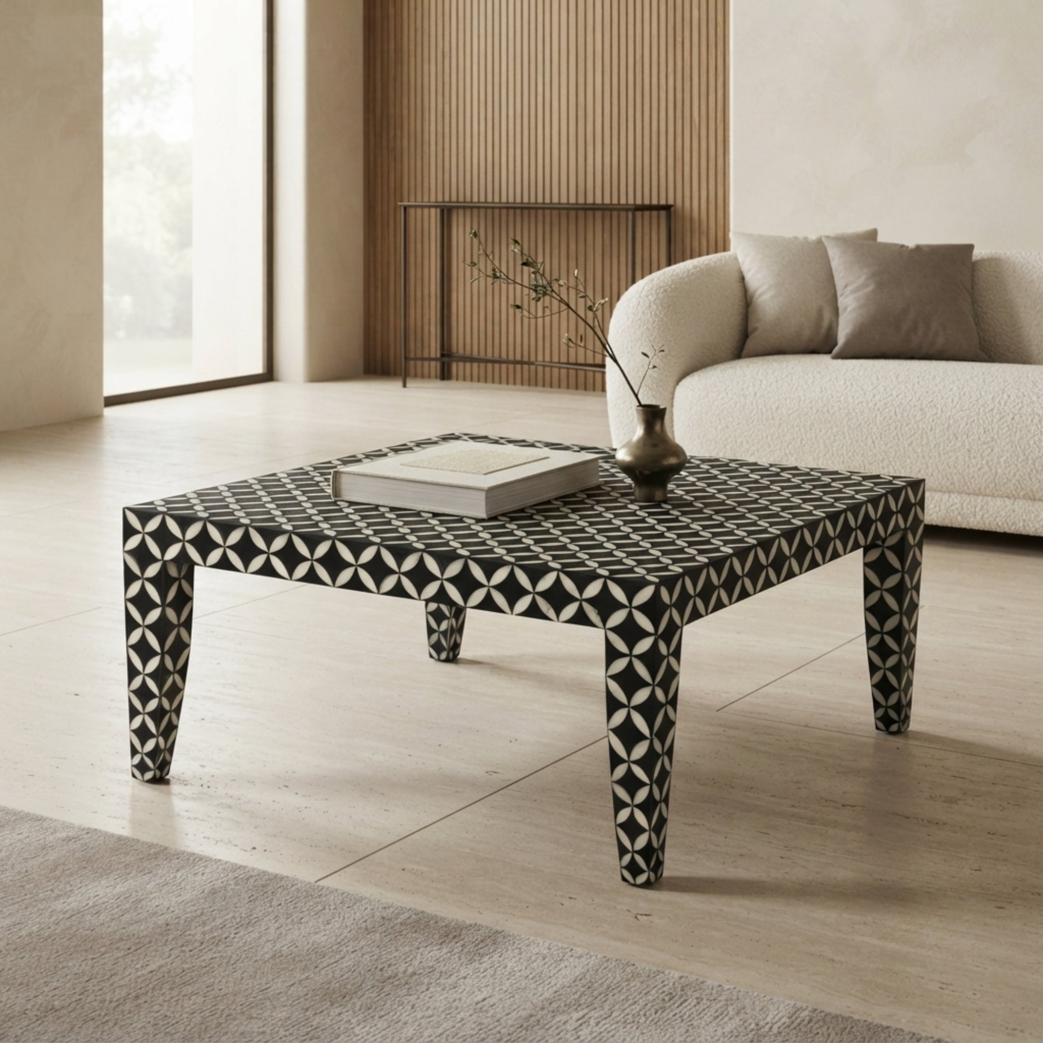 A square coffee table with a black and white geometric bone-inlay pattern, styled in a modern living room next to a cream bouclé sofa.