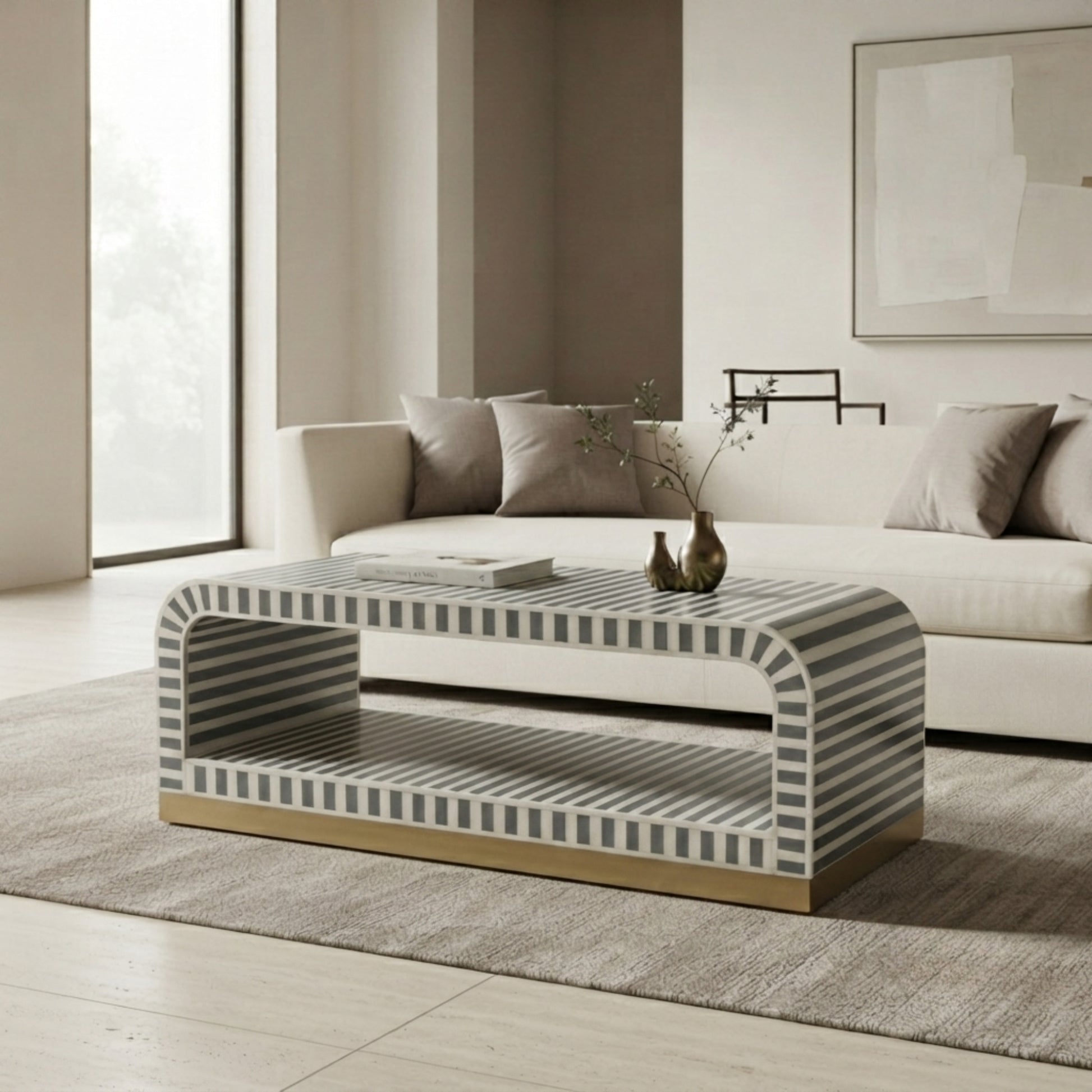 A modern rectangular coffee table with a striped gray and white bone inlay top and base, supported by a gold-finished wooden frame, set in a contemporary living room next to a white sofa.
