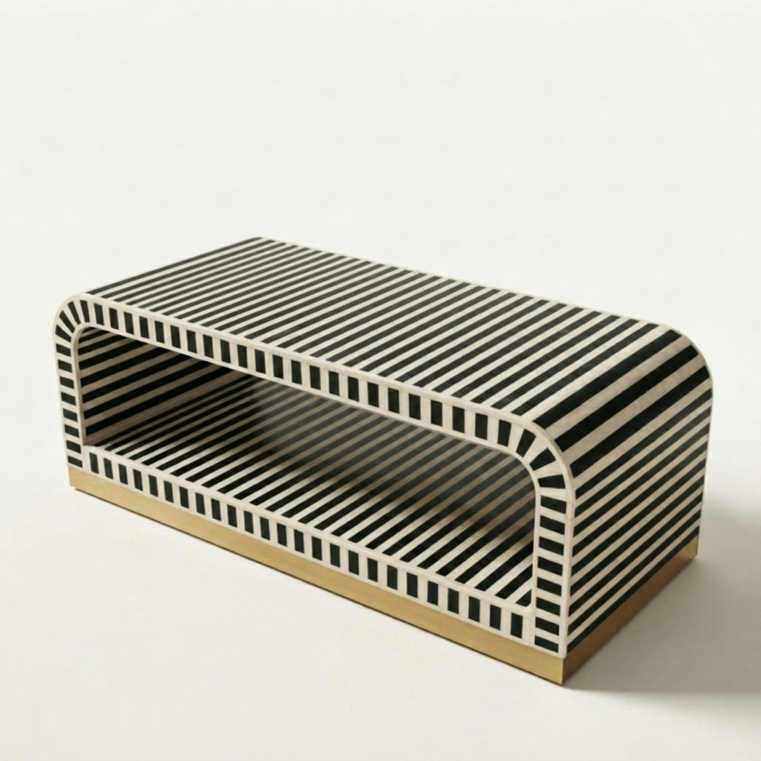 A modern rectangular coffee table with a black and white striped pattern and a gold-toned base, styled in a minimalist living room next to a white sofa.
