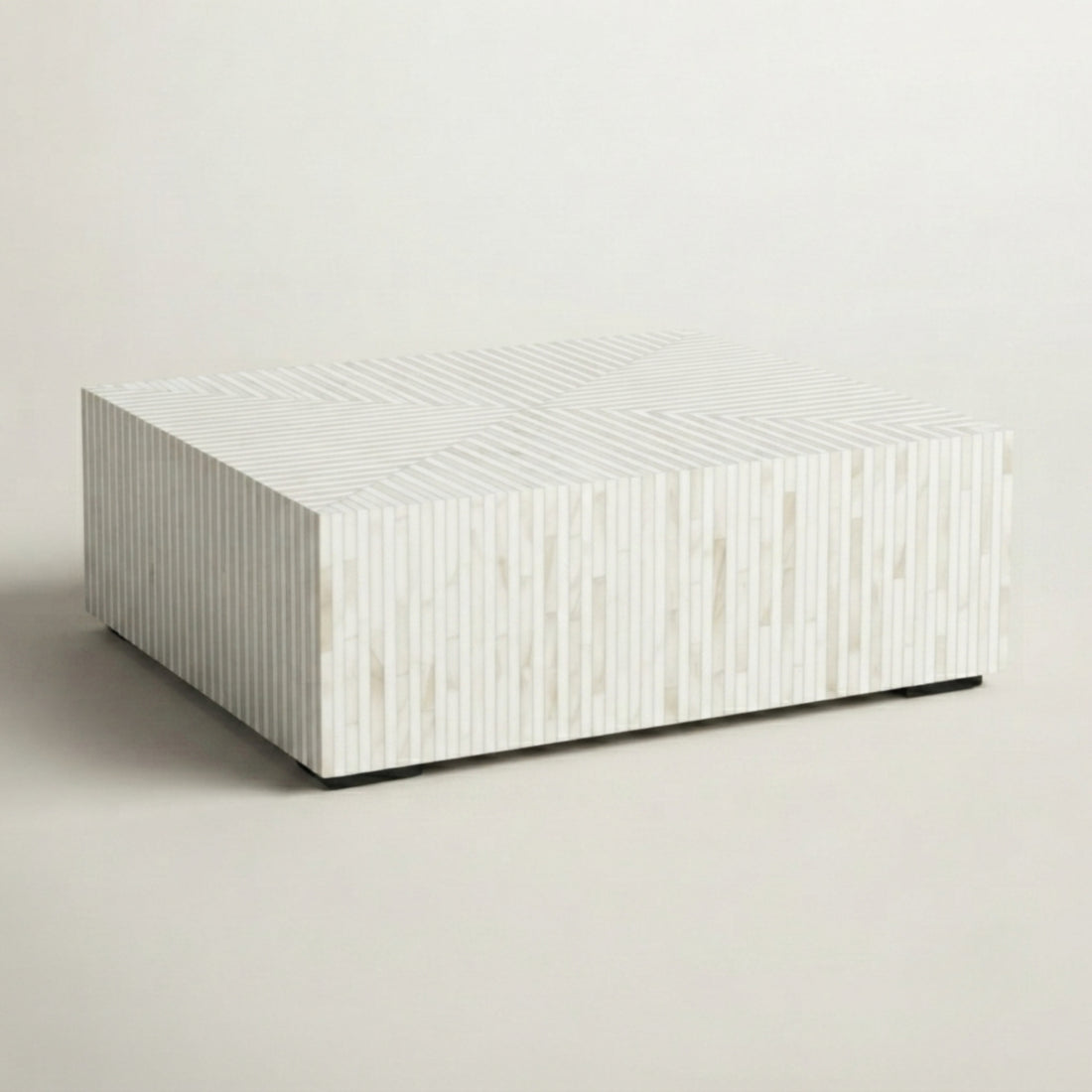 A modern square coffee table with a textured white and light beige wood-grain finish, styled in a living room setting with a cream sofa and geometric wood flooring.