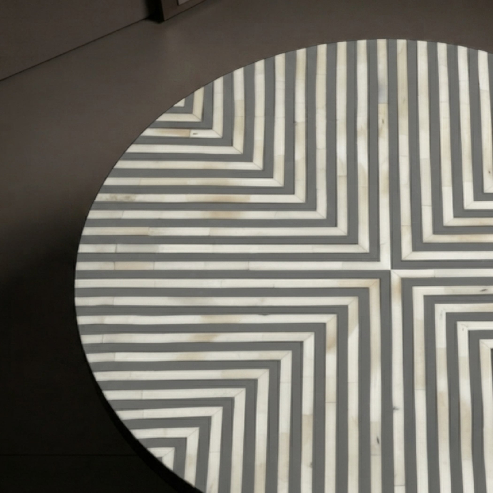 A close-up of a round table or tray featuring a geometric chevron pattern made from alternating off-white and dark gray inlay strips.
