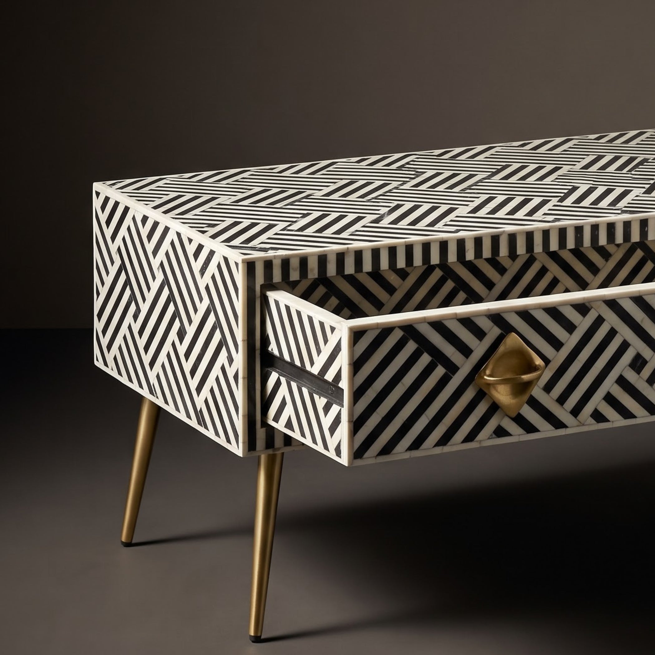 A modern sideboard or console table with a black and white geometric bone-inlay pattern, featuring tapered gold metal legs and a matching gold geometric drawer pull.