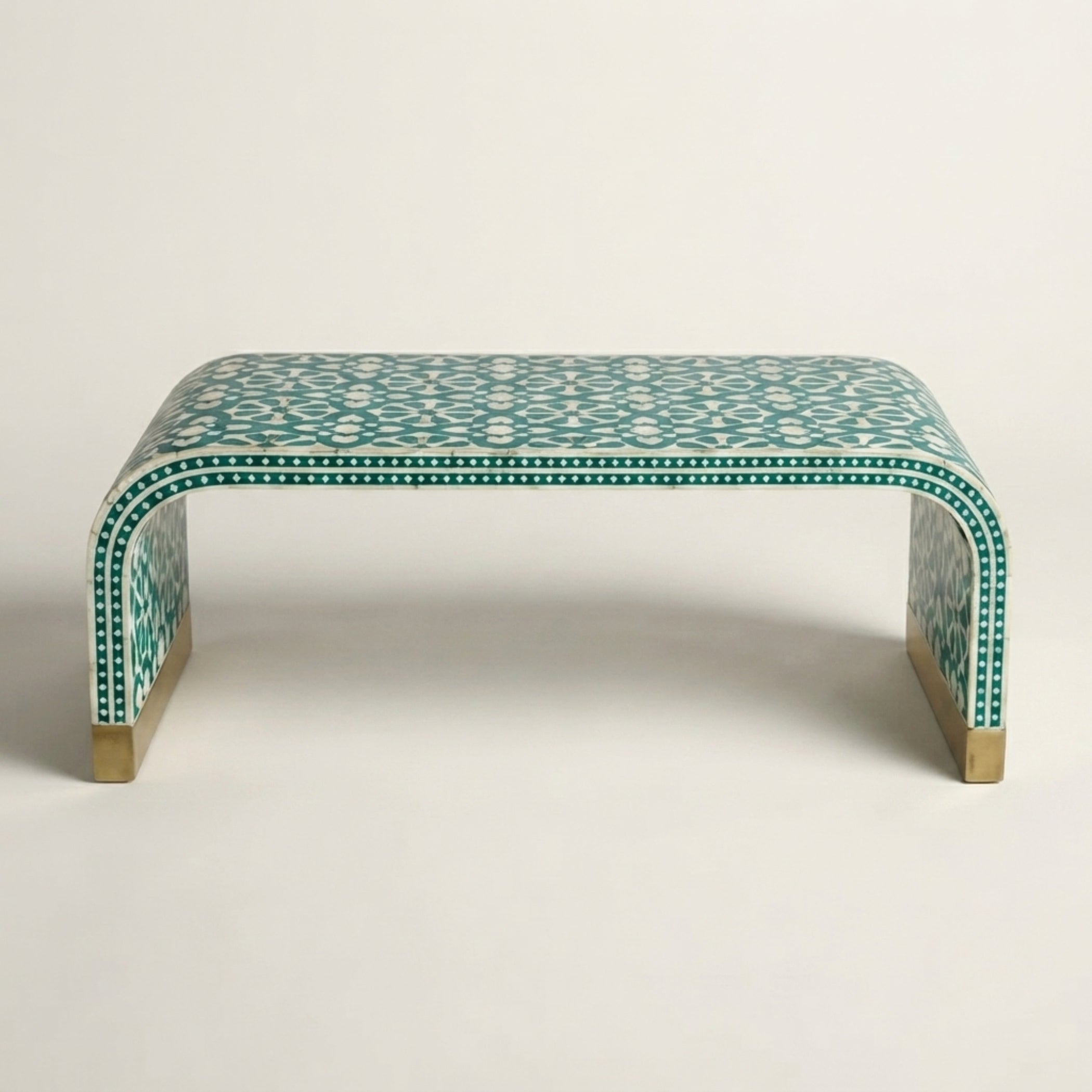 A curved bench with a green and white geometric bone-inlay pattern and brass-colored legs, photographed against a neutral light gray background.