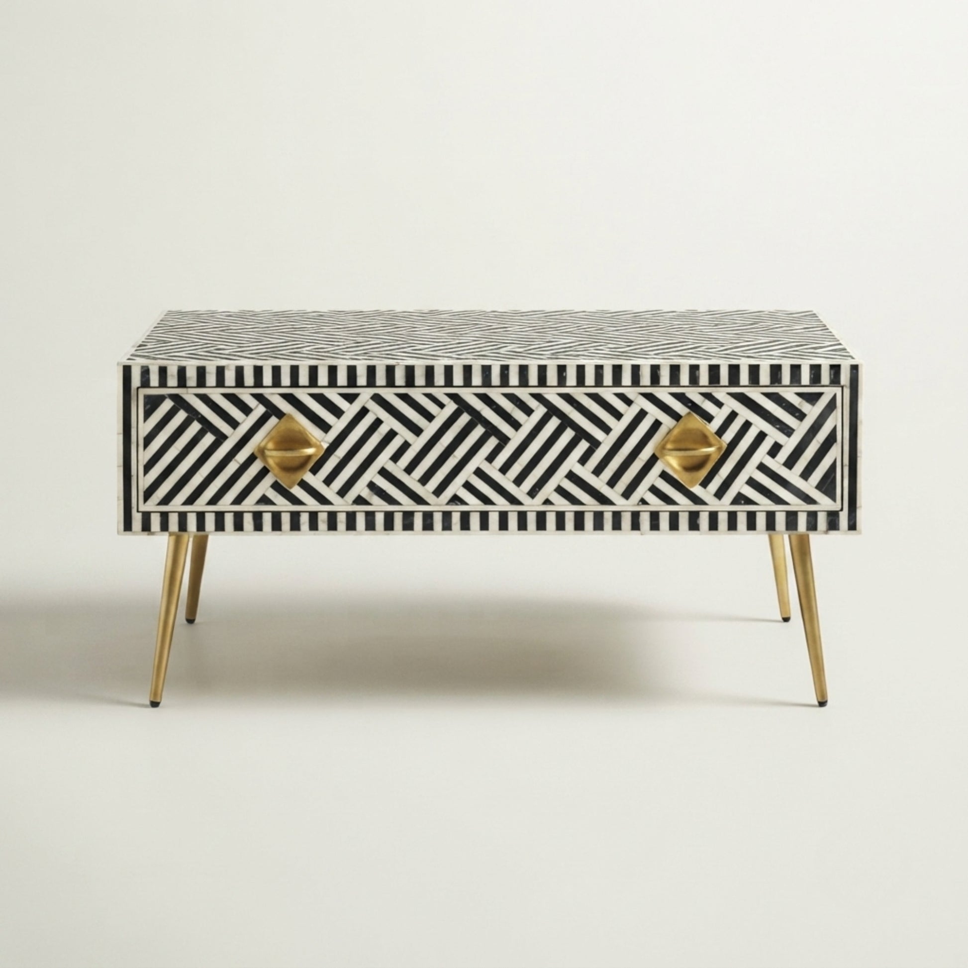 A mid-century modern two-drawer console table featuring a black and white geometric bone-inlay pattern, gold-finished metal drawer pulls, and tapered gold legs, set against a plain off-white background.