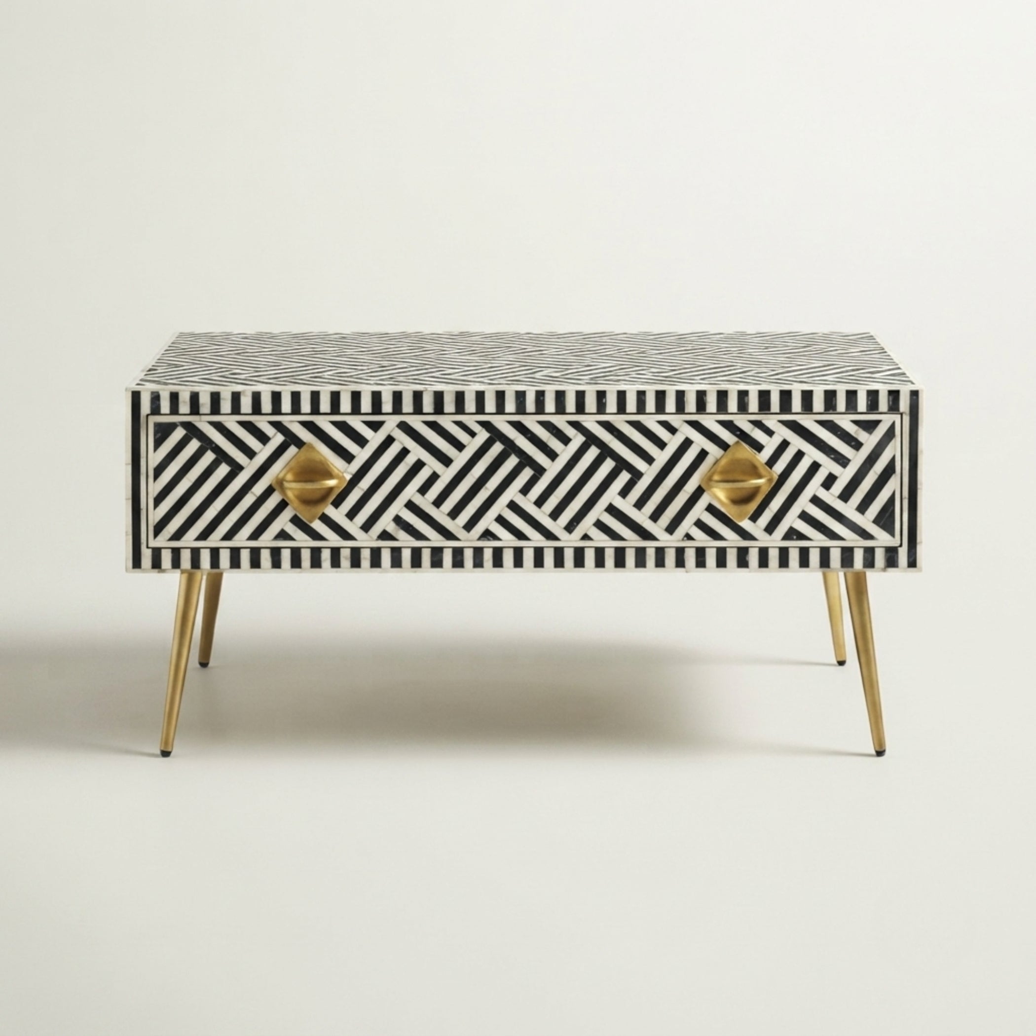 A mid-century modern two-drawer console table featuring a black and white geometric bone-inlay pattern, gold-finished metal drawer pulls, and tapered gold legs, set against a plain off-white background.