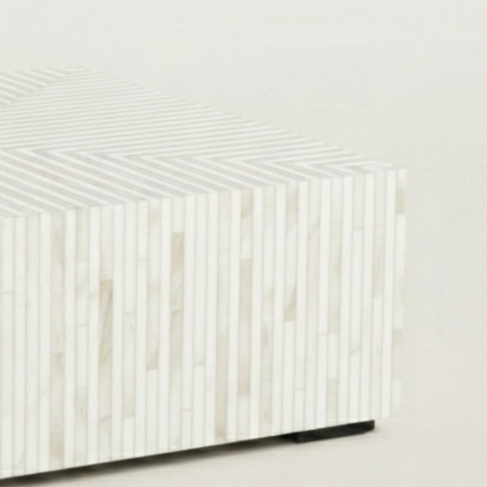 A close-up of a modern rectangular side table or stool with a white and beige striped bone-in-shell striped pattern, featuring a small black base leg.
