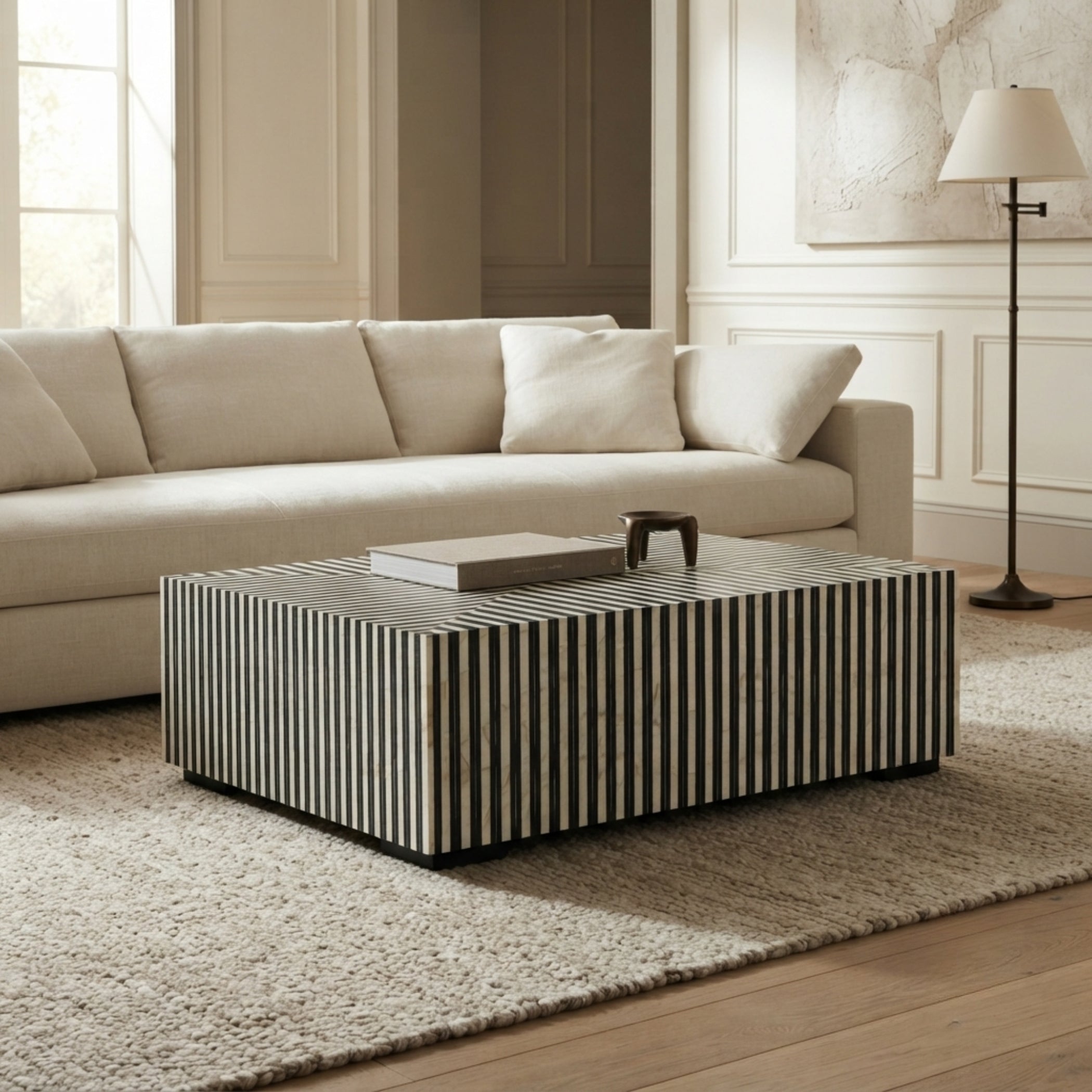 A modern rectangular coffee table with vertical black and cream stripes, styled in a bright living room next to a cream sofa and a floor lamp.