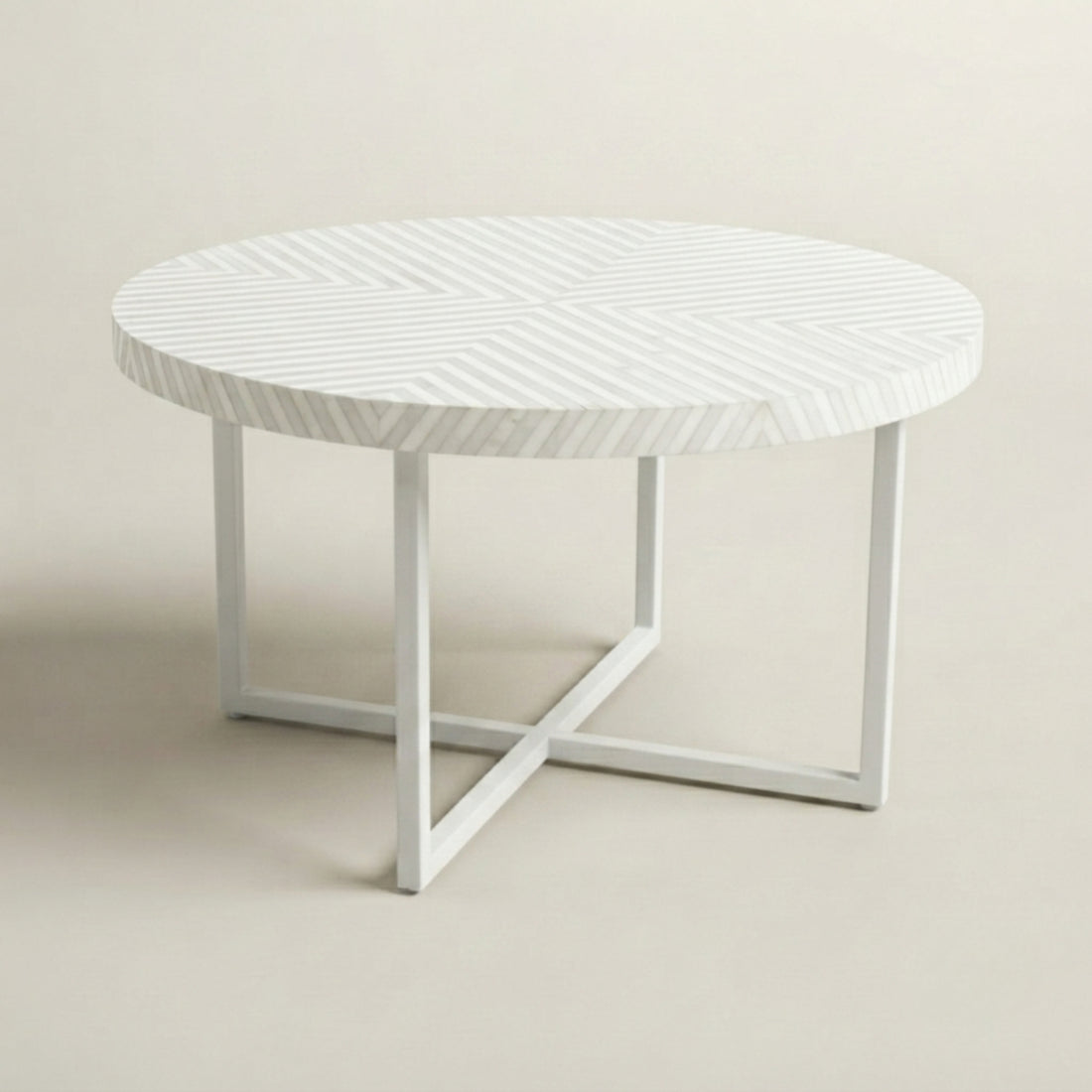 A round white coffee table with a textured chevron-patterned top and white metal legs, styled in a bright, modern living room next to a cream boucle sofa.