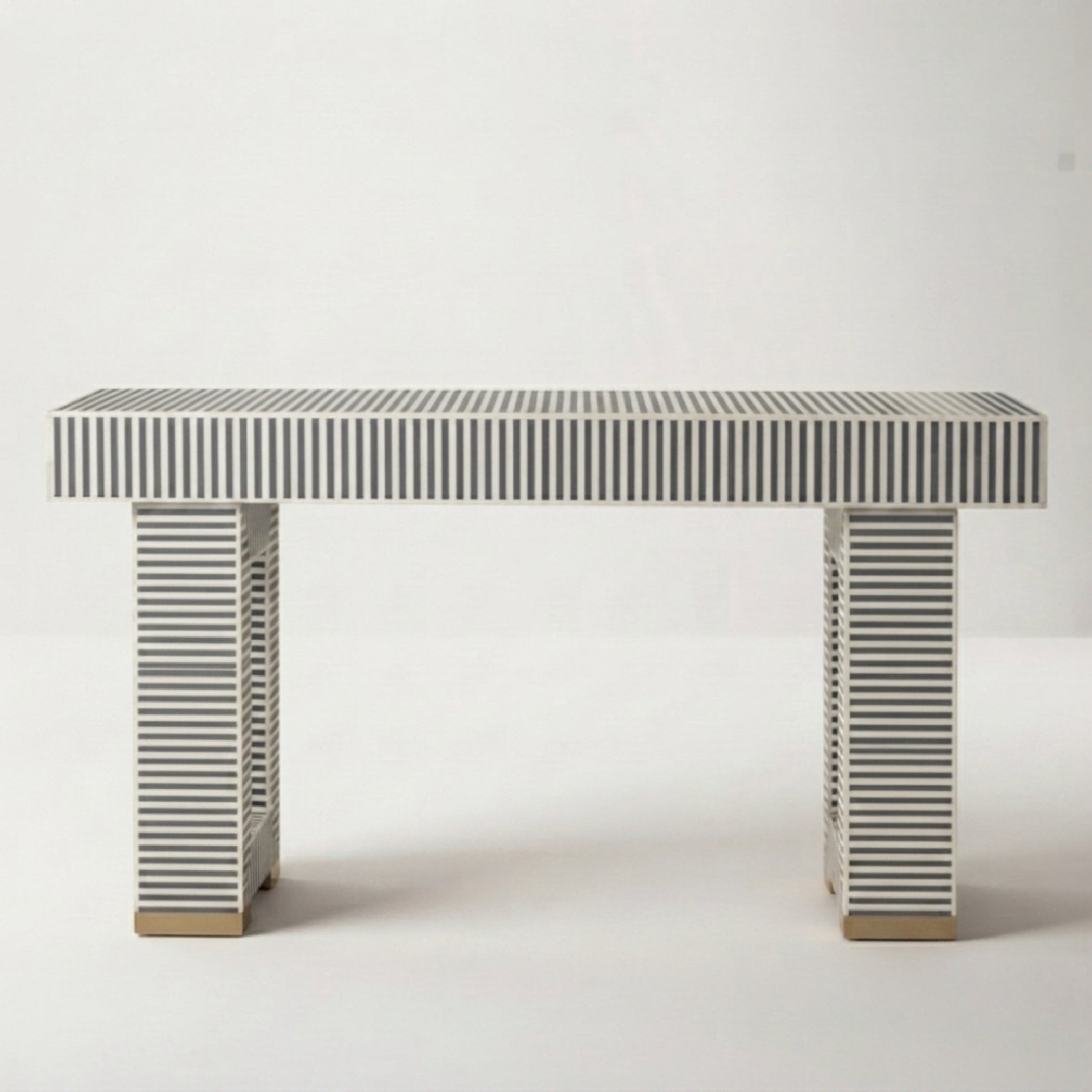 A modern console table with a rectangular top and two matching legs, both covered in narrow vertical black and white stripes, with small gold-toned metal feet at the bottom, set against a plain light gray background.