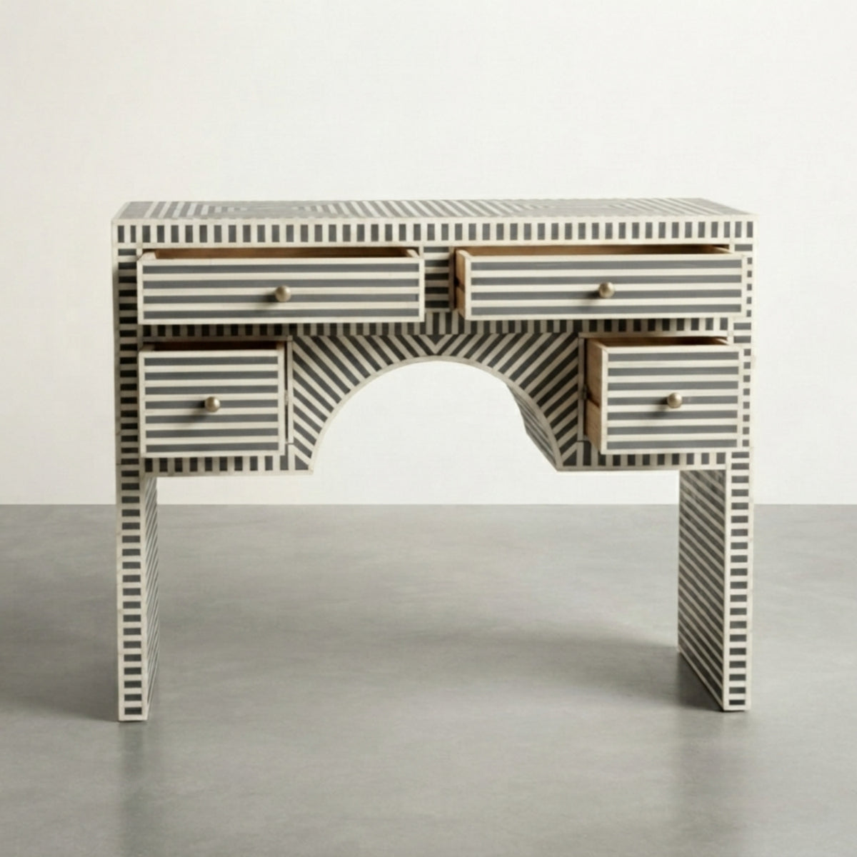 A bone-and-wood writing desk with a black and white striped bone inlay pattern, featuring a central arch opening and four drawers with brass handles, set against a neutral studio background.