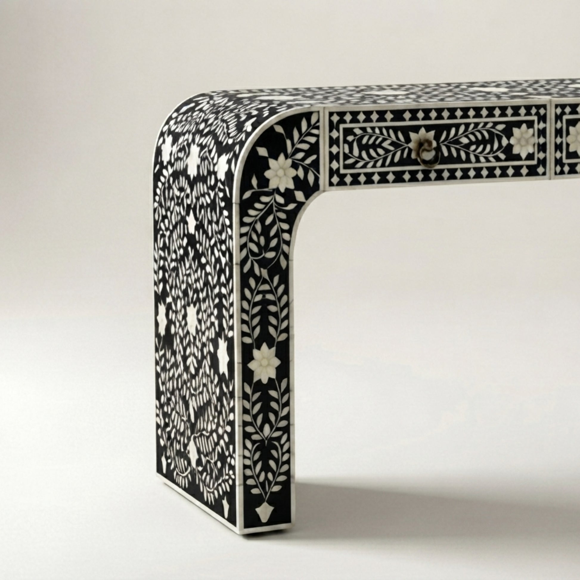 A close-up studio shot of a black and white bone-inlay table leg and drawer front, showing intricate floral and geometric patterns on a light neutral background.