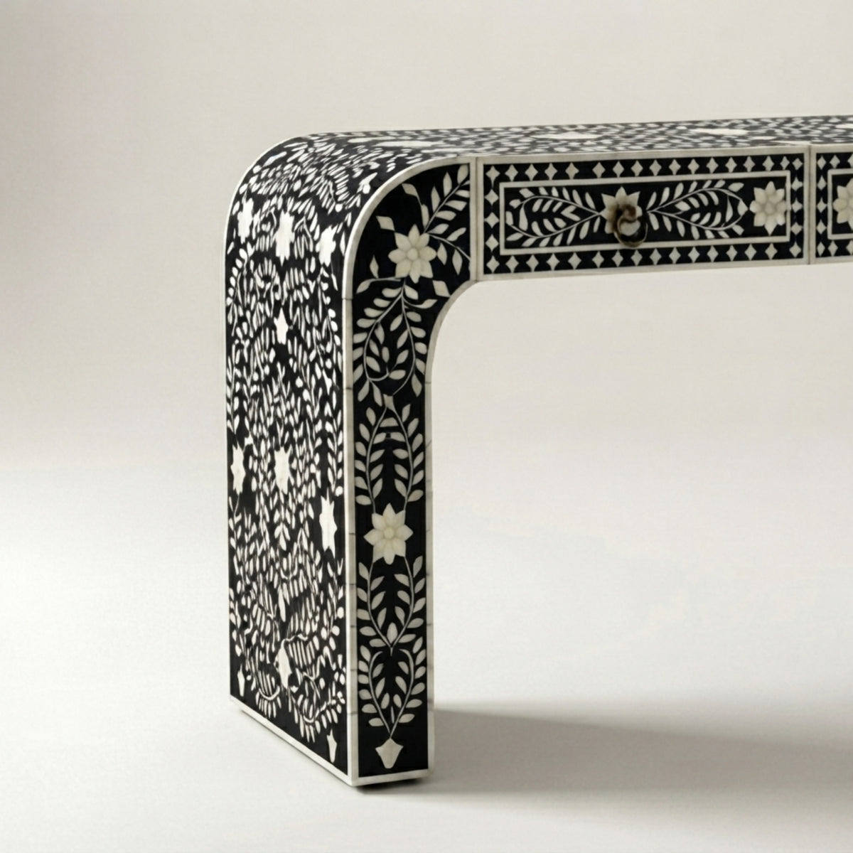 A close-up studio shot of a black and white bone-inlay table leg and drawer front, showing intricate floral and geometric patterns on a light neutral background.