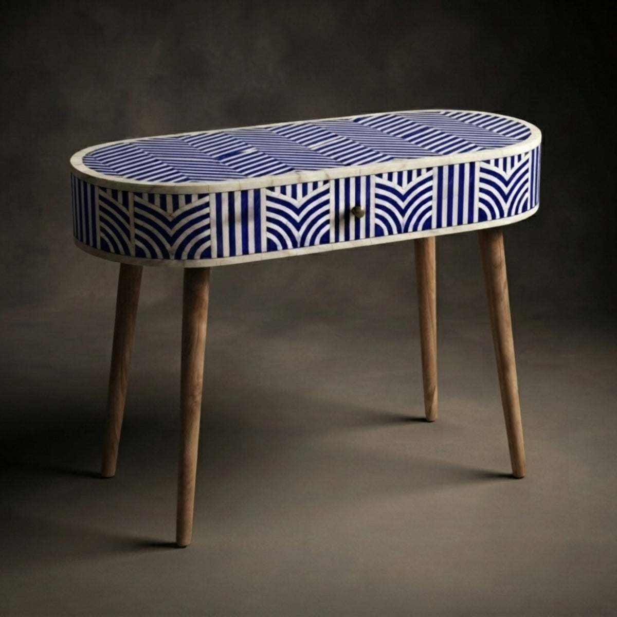 An oval console table with a blue and white patterned bone inlay top and sides, supported by four tapered natural wood legs, set against a dark gray studio background.