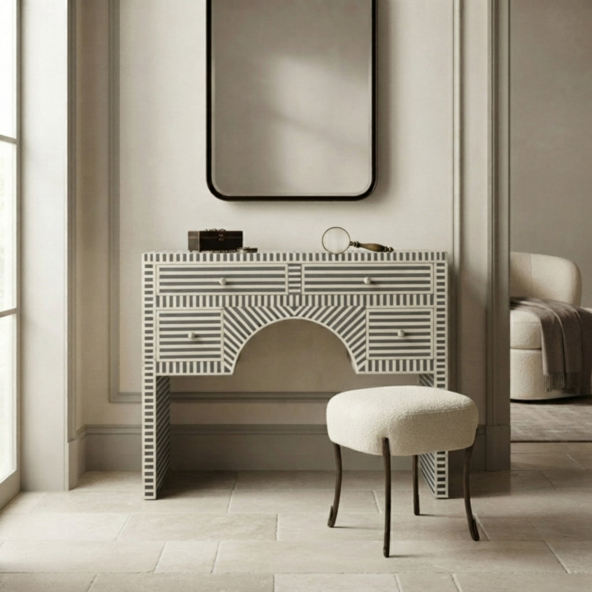 A white and gray striped bone-patterned vanity console table with a matching upholstered stool, set in a bright, modern room under a large black-framed mirror.
