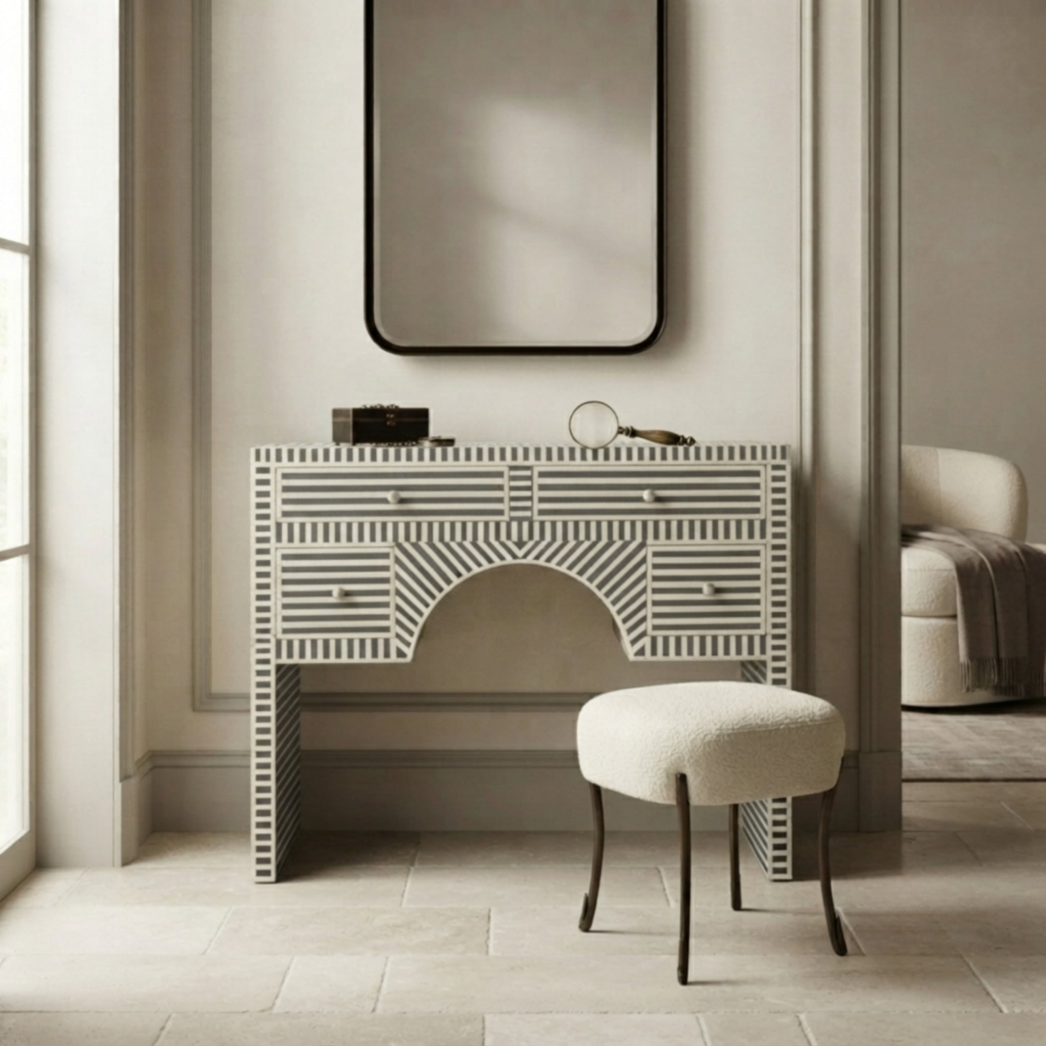 A white and gray striped bone-patterned vanity console table with a matching upholstered stool, set in a bright, modern room under a large black-framed mirror.