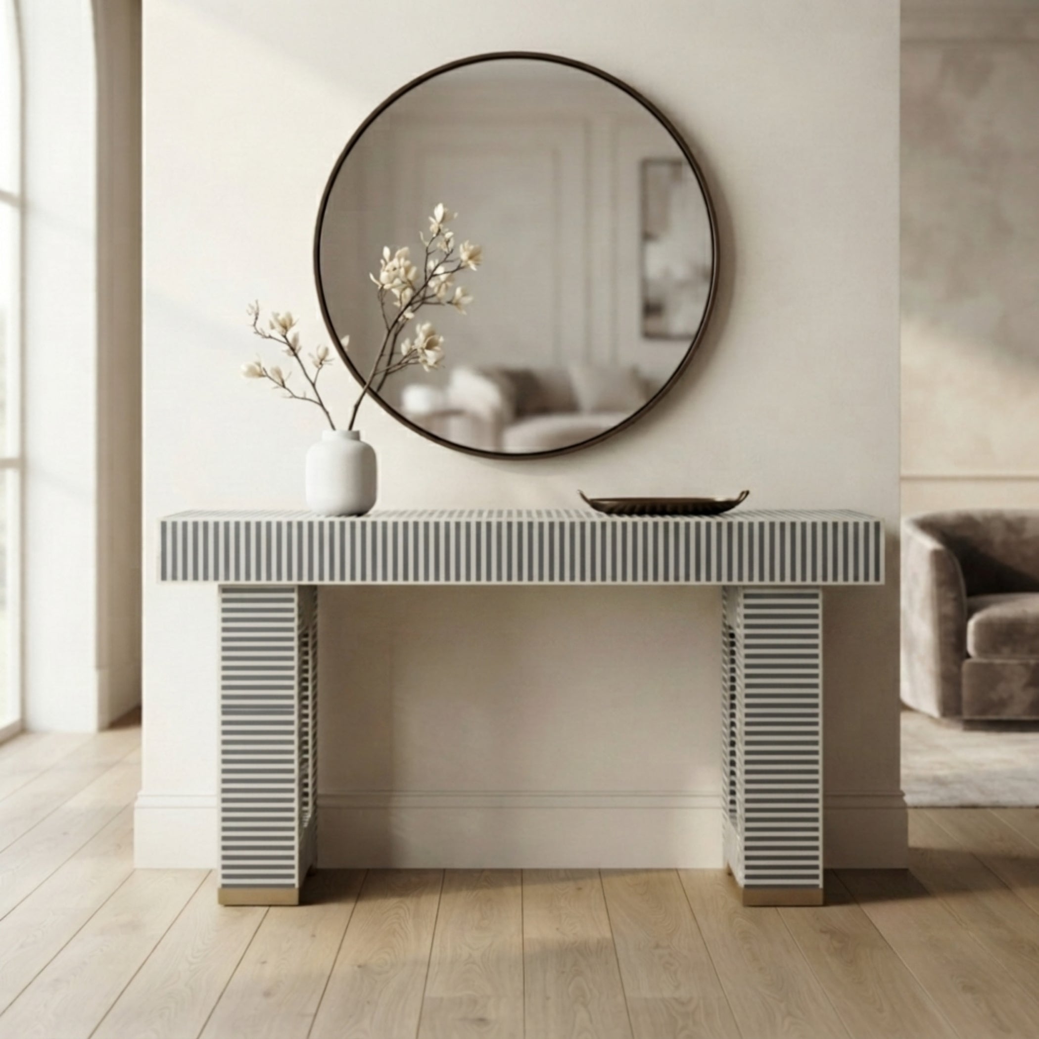 A modern console table with a gray and white striped patterned top and matching fluted legs, styled in a bright, minimalist room with a round wall mirror and a white vase of branches.