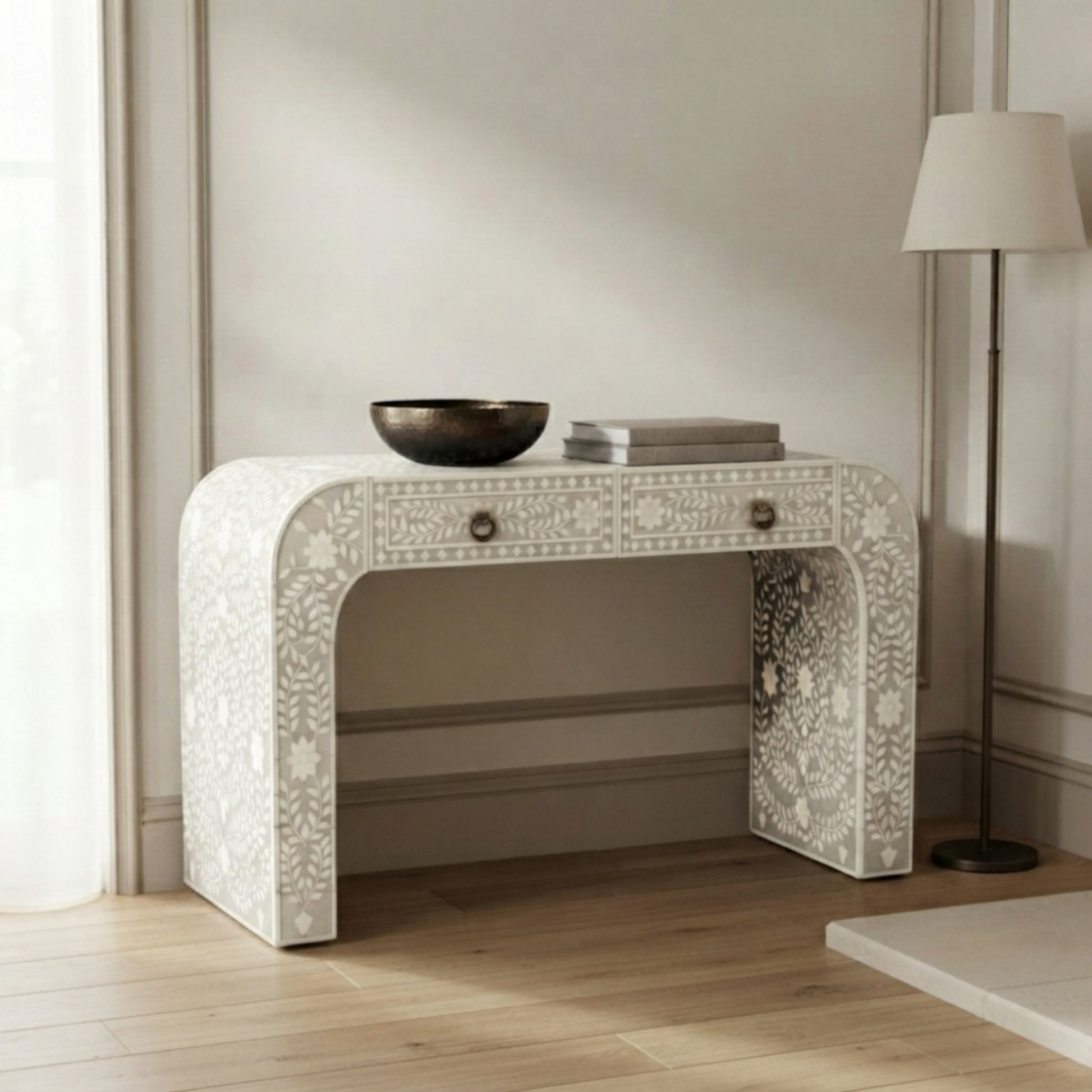 An ornate white bone-inlay console table with a single drawer and two legs, styled in a bright room with a floor lamp and wooden floor.