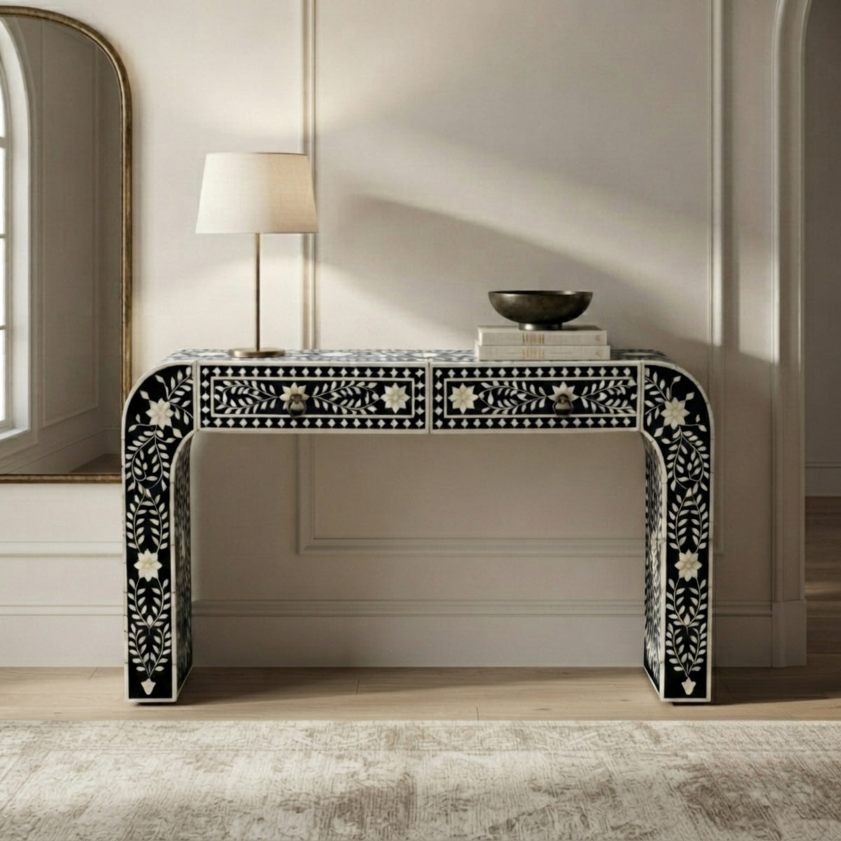 A black and white bone-inlay console table with two drawers, styled in a bright, modern room with a table lamp and a bowl on top.