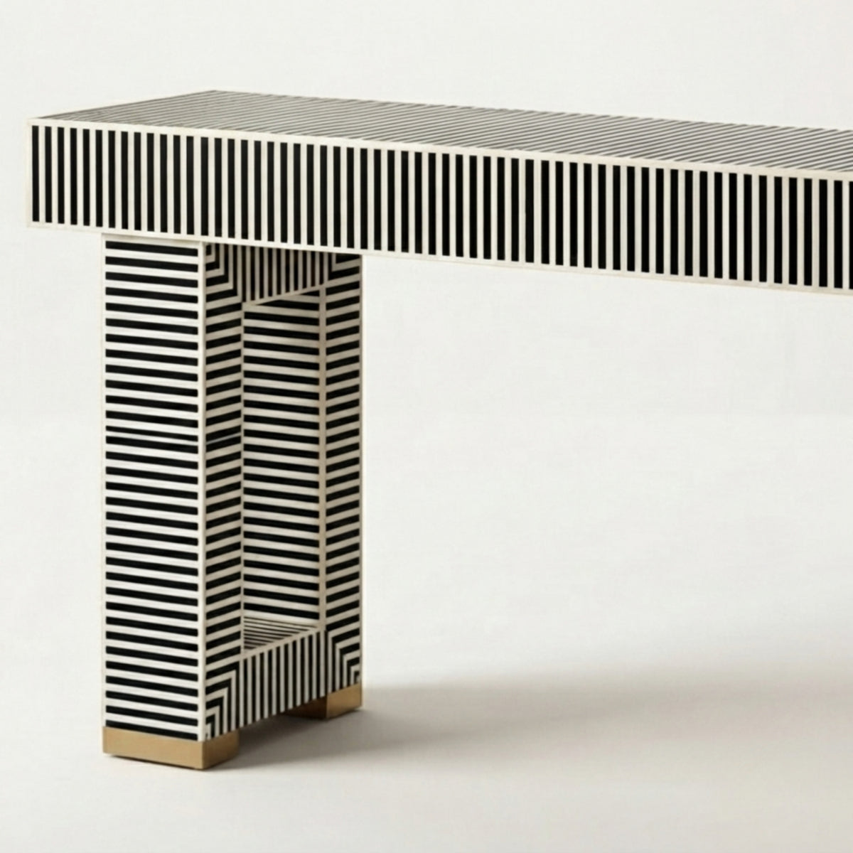 A modern console table with a rectangular top and column-style legs, both covered in black and white vertical stripes, with small gold-toned metal feet at the bottom, shown on a light gray studio background.