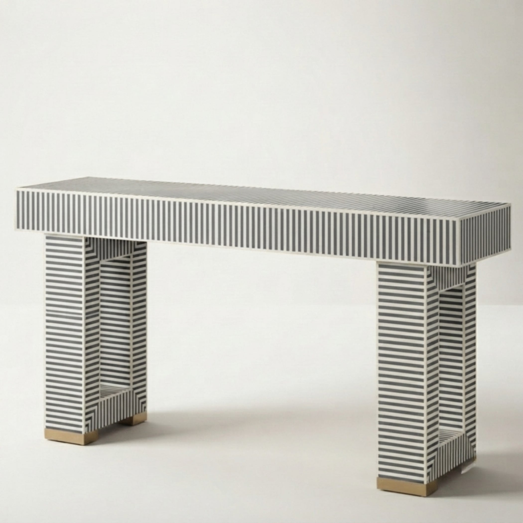 A modern console table with a rectangular top and two matching legs, both covered in narrow black and white striped bone inlay, finished with small gold-toned wooden feet.