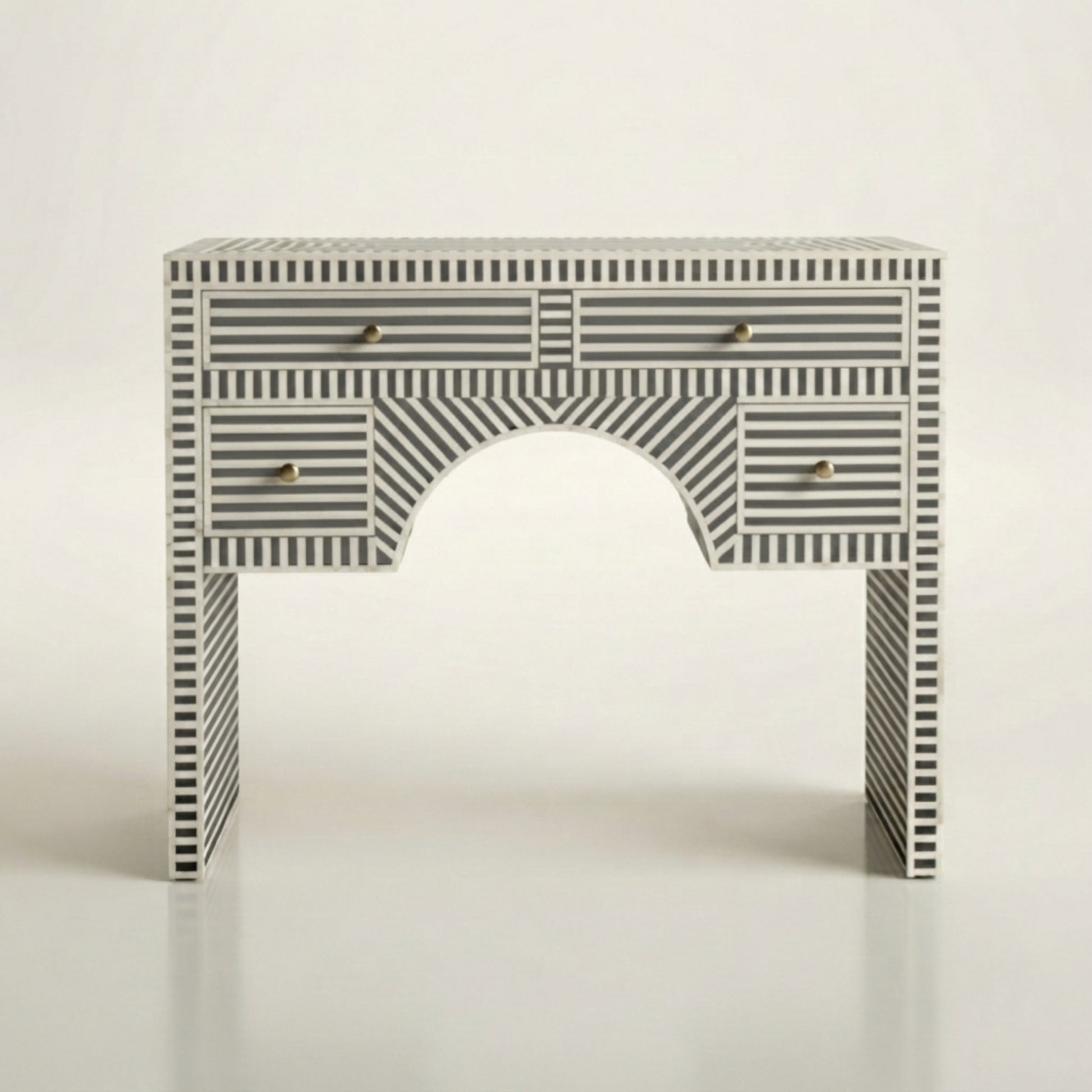 A console table with a black and white striped bone-inlay pattern, featuring an arched center panel and three drawers with small gold pull handles, set against a plain light background.