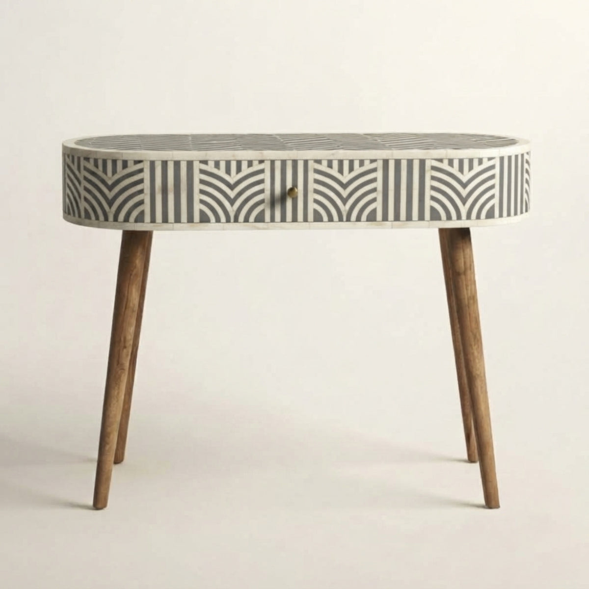 An oval console table featuring a bone-inlay patterned top and drawer front in black and off-white, supported by four tapered medium-brown wooden legs, set against a plain light background.