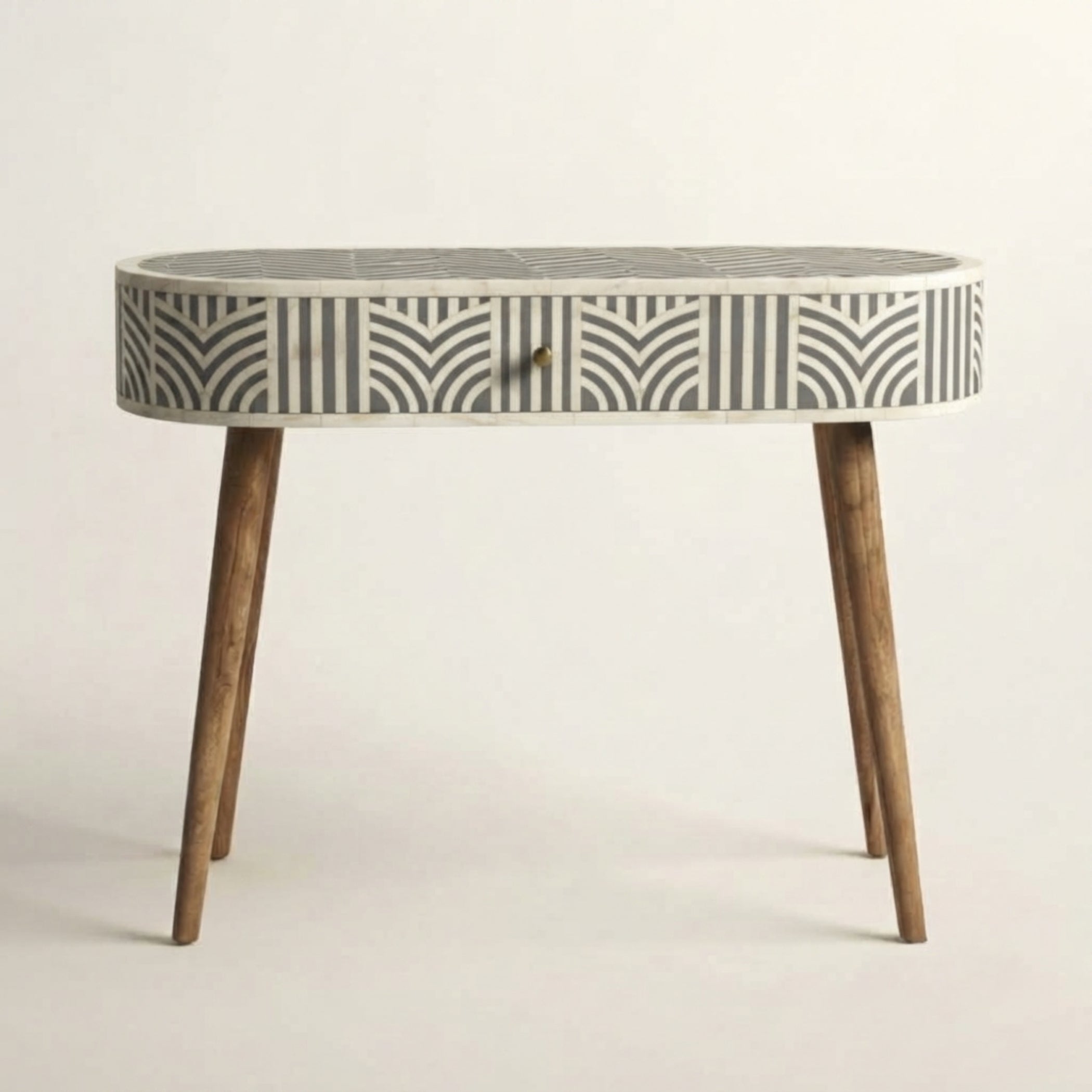 An oval console table featuring a bone-inlay patterned top and drawer front in black and off-white, supported by four tapered medium-brown wooden legs, set against a plain light background.