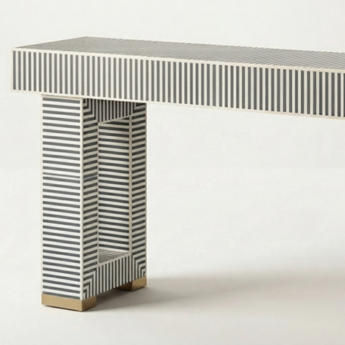 A modern console table with a rectangular top and single column base, both decorated with a black and white striped bone-inlay pattern, finished with gold-toned block feet, shown against a plain white background.