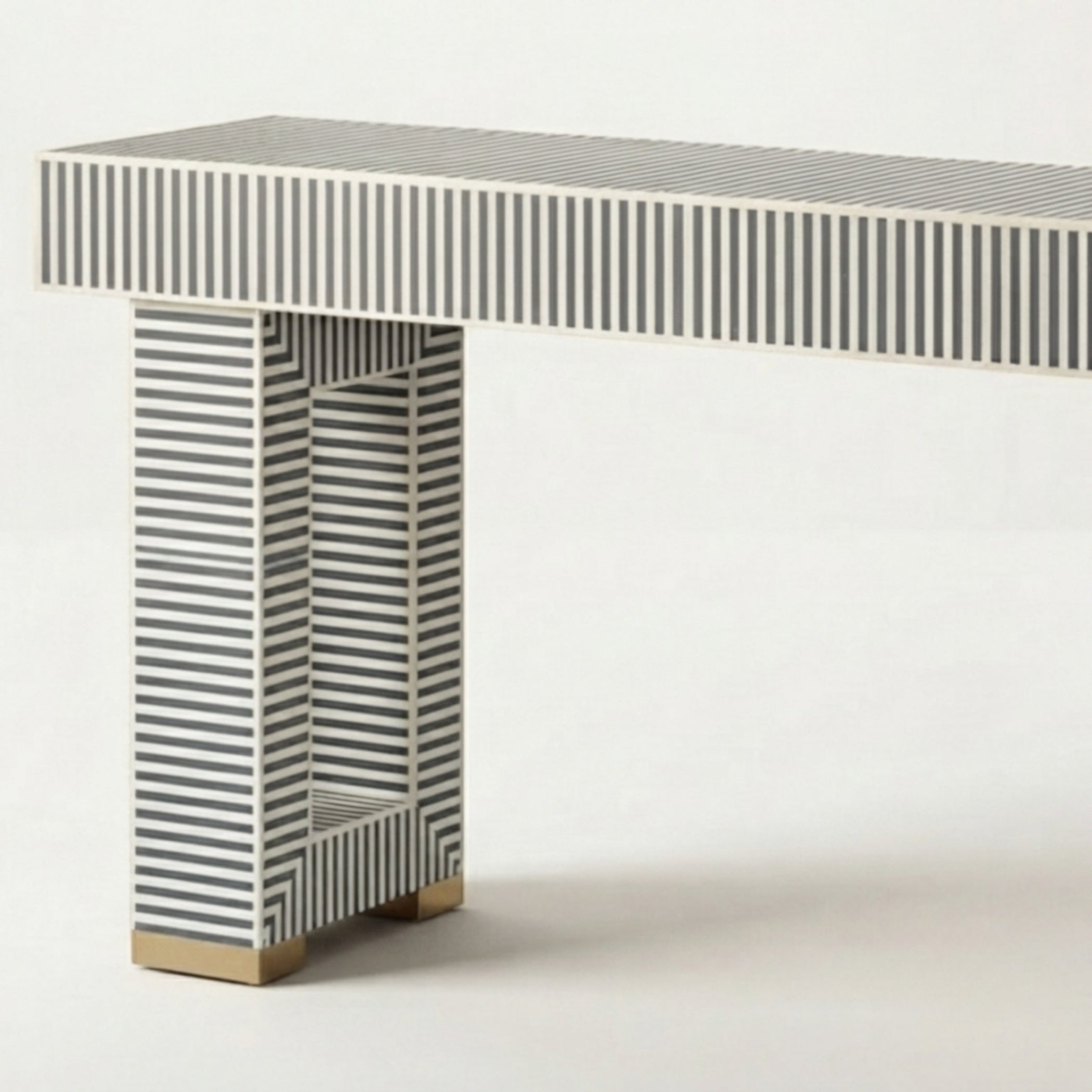 A modern console table with a rectangular top and single column base, both decorated with a black and white striped bone-inlay pattern, finished with gold-toned block feet, shown against a plain white background.