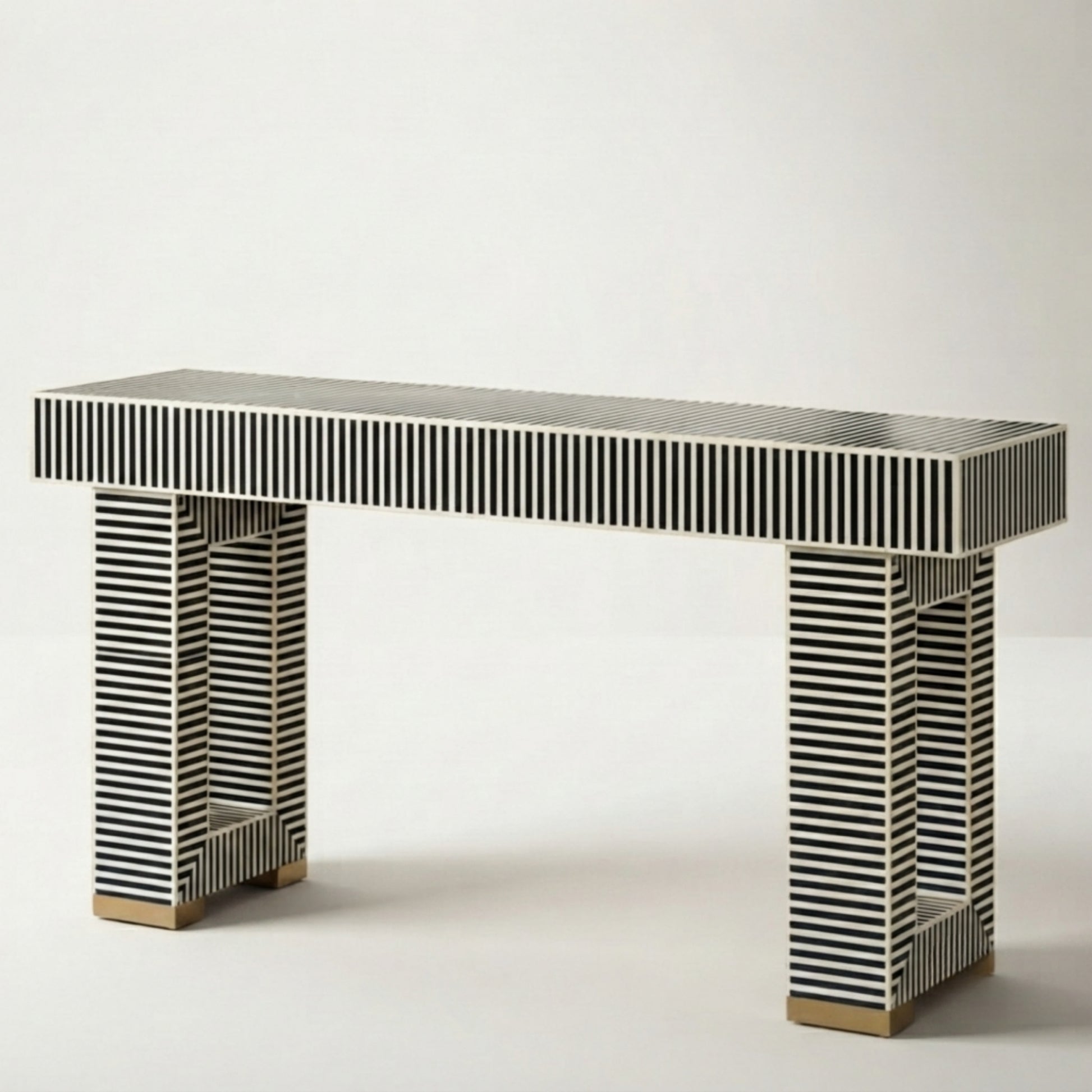 A modern console table with a rectangular top and two open rectangular legs, both covered in black and white striped bone inlay, finished with small gold-toned metal feet, shown on a light gray background.