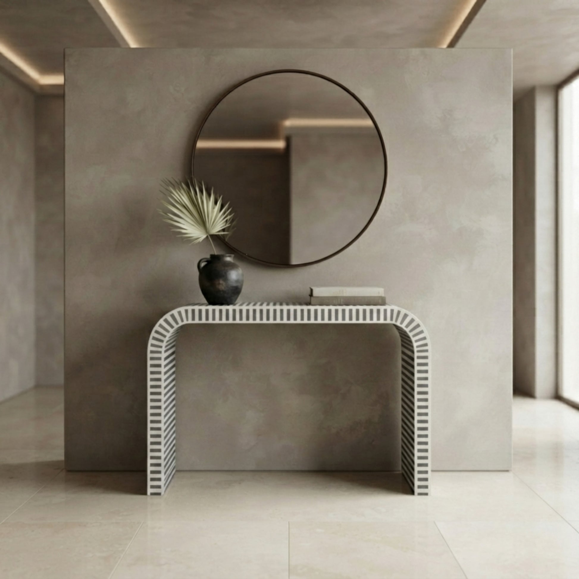A modern minimalist interior scene featuring a sculptural white console table with a ribbed, wave-like front and base, set against a textured gray wall with a round black-framed mirror and a small black vase with a dried palm frond.