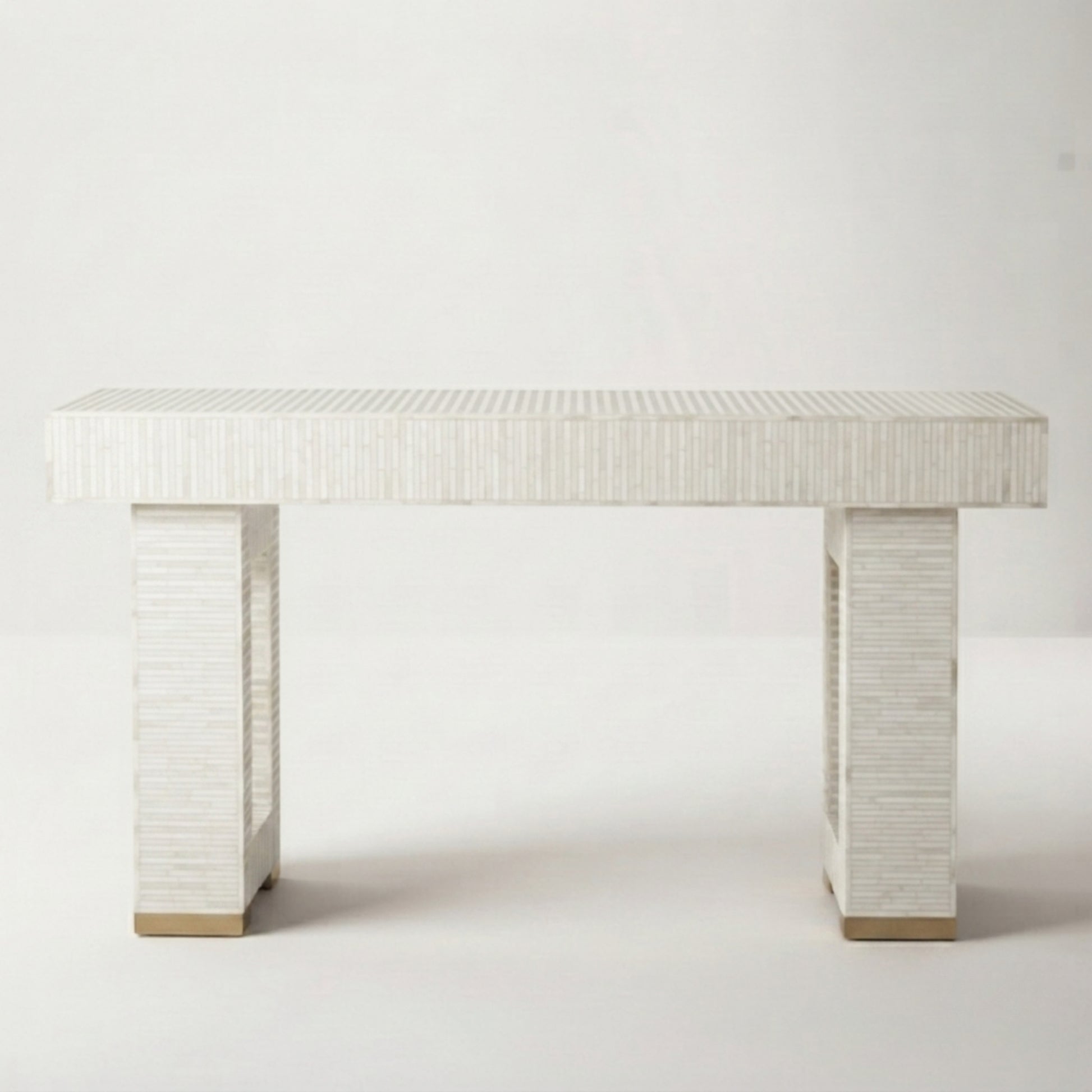 A modern console table with a textured white shell-look rectangular top and two matching block legs, finished with small gold-toned metal caps at the base, shown against a plain light gray studio background.