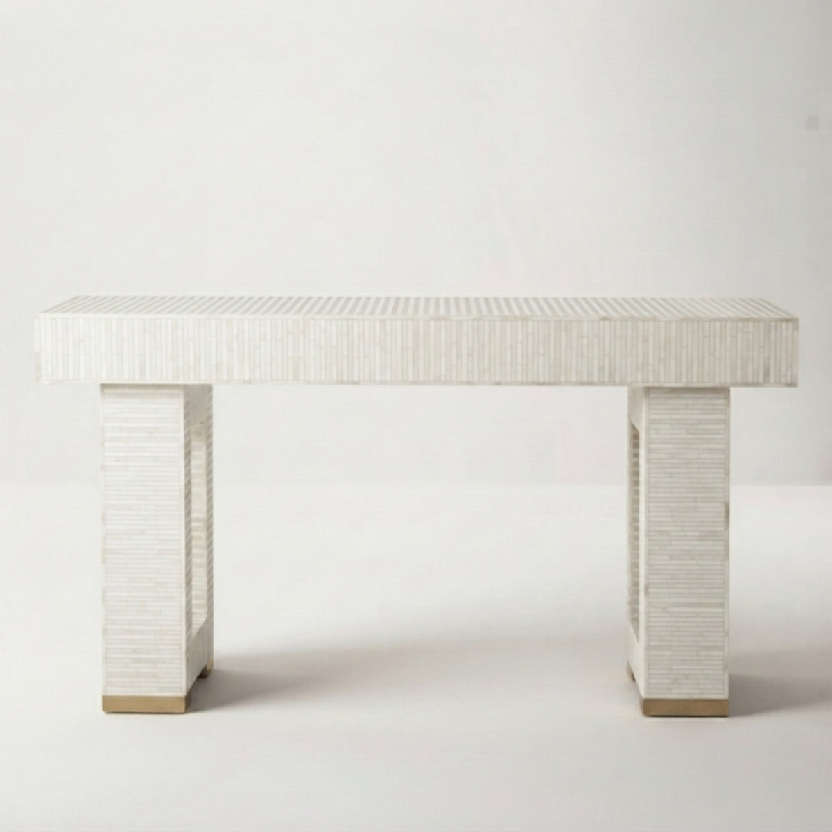 A modern console table with a textured white shell-look rectangular top and two matching block legs, finished with small gold-toned metal caps at the base, shown against a plain light gray studio background.
