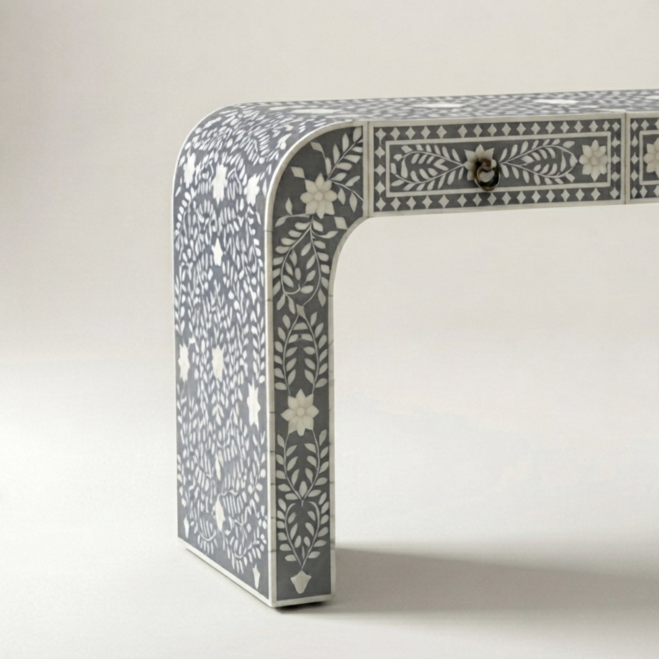 A close-up of a gray and white bone-inlay table leg and drawer front, showing intricate floral and geometric patterns on a light background.