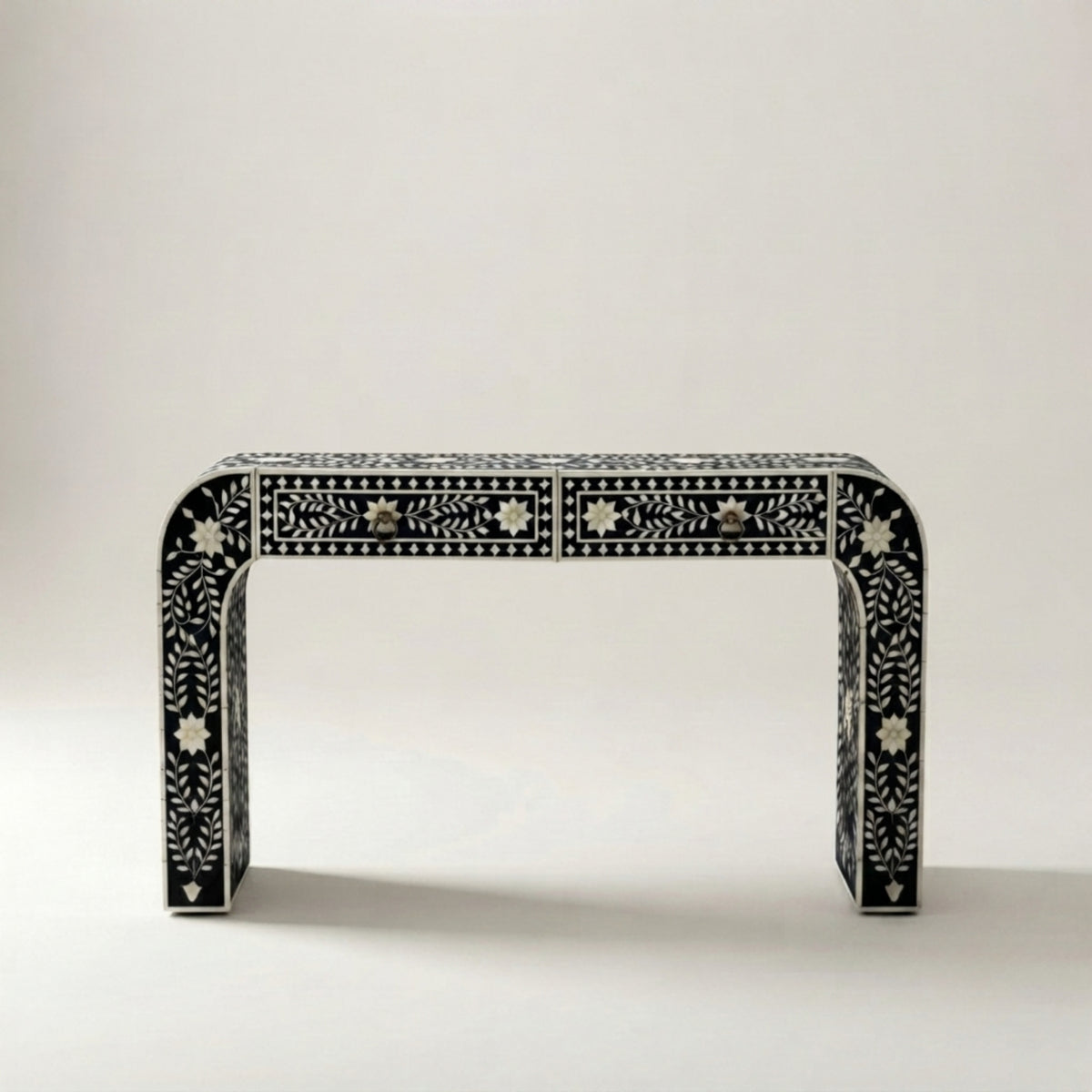 A black console table with intricate white bone-inlay patterns and three drawers, photographed against a neutral light gray background.