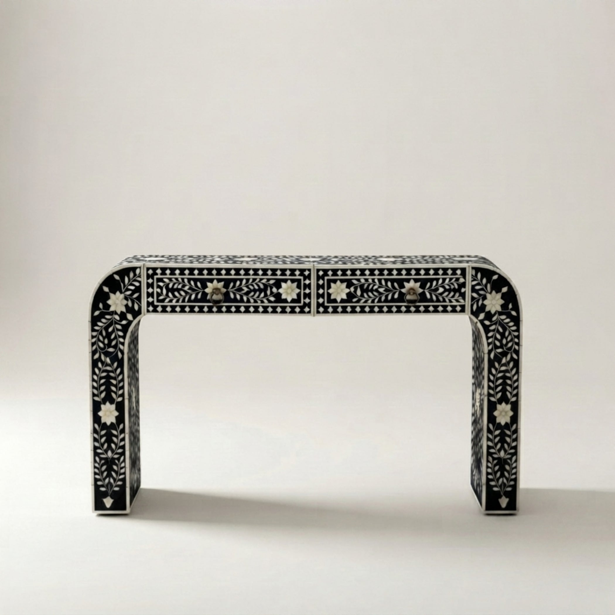 A black console table with intricate white bone-inlay patterns and three drawers, photographed against a neutral light gray background.