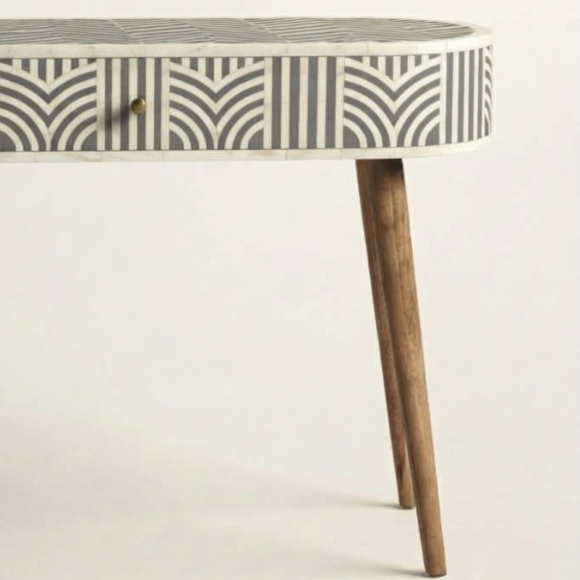 A close-up of a table with a white and gray geometric inlay pattern on the top and drawer front, supported by two tapered wooden legs, against a plain off-white background.