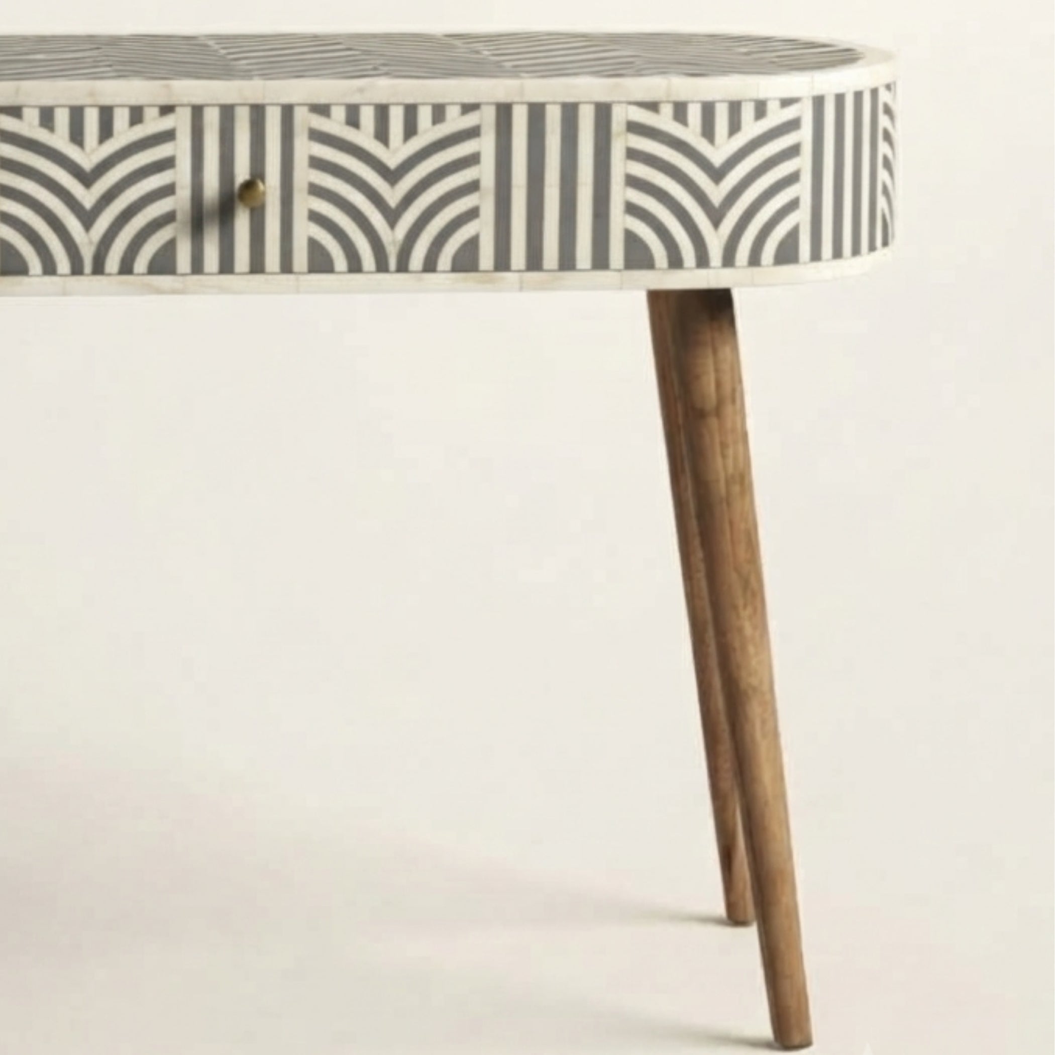 A close-up of a table with a white and gray geometric inlay pattern on the top and drawer front, supported by two tapered wooden legs, against a plain off-white background.