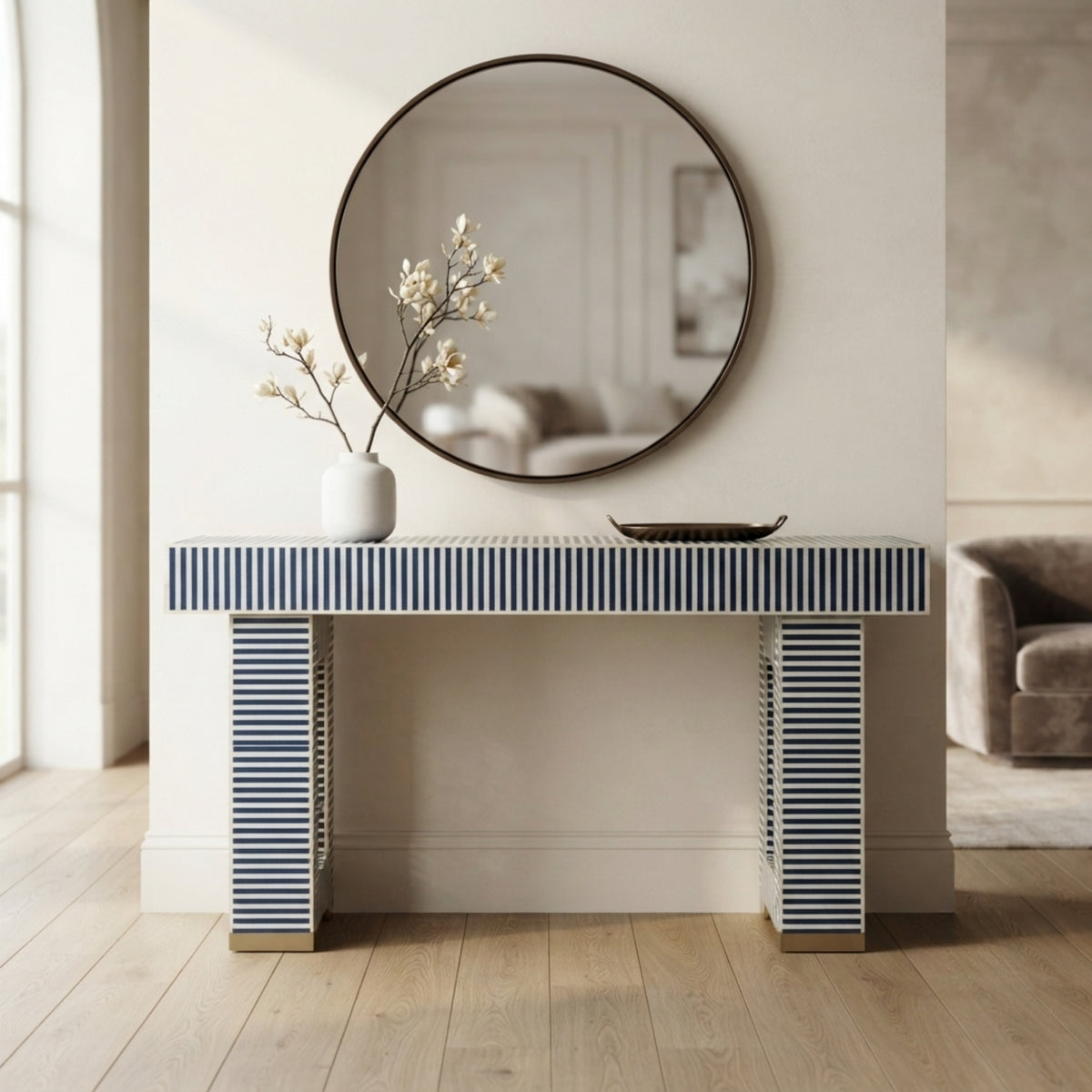 A modern console table with a blue and white striped pattern, styled in a bright, minimalist living room under a round wall mirror.