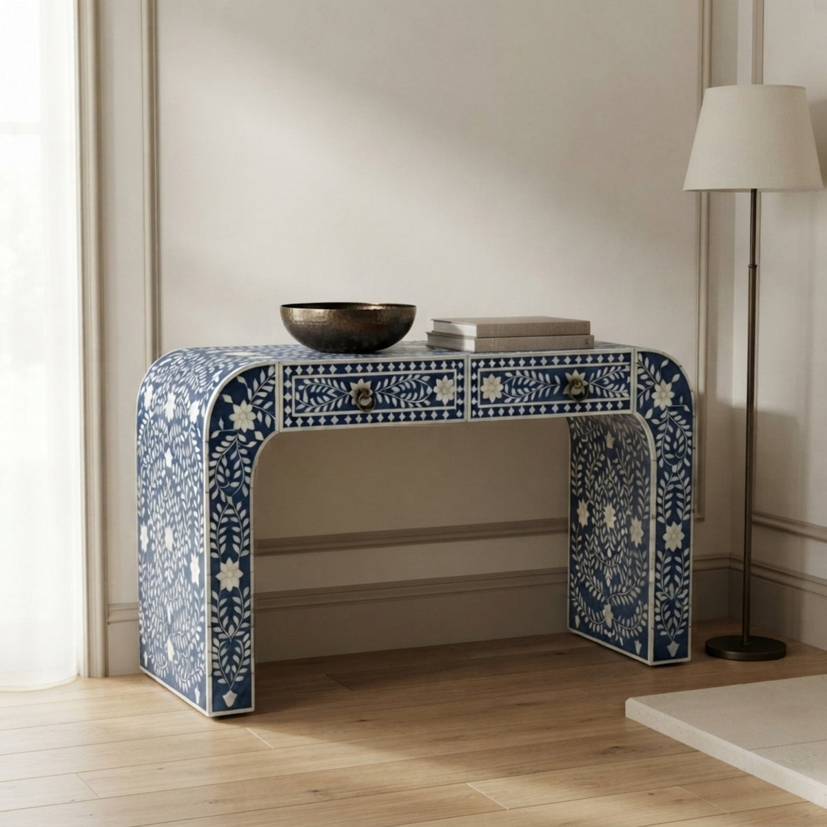 A blue and white bone-inlay console table styled in a bright room with a floor lamp, books, and a bowl on top.