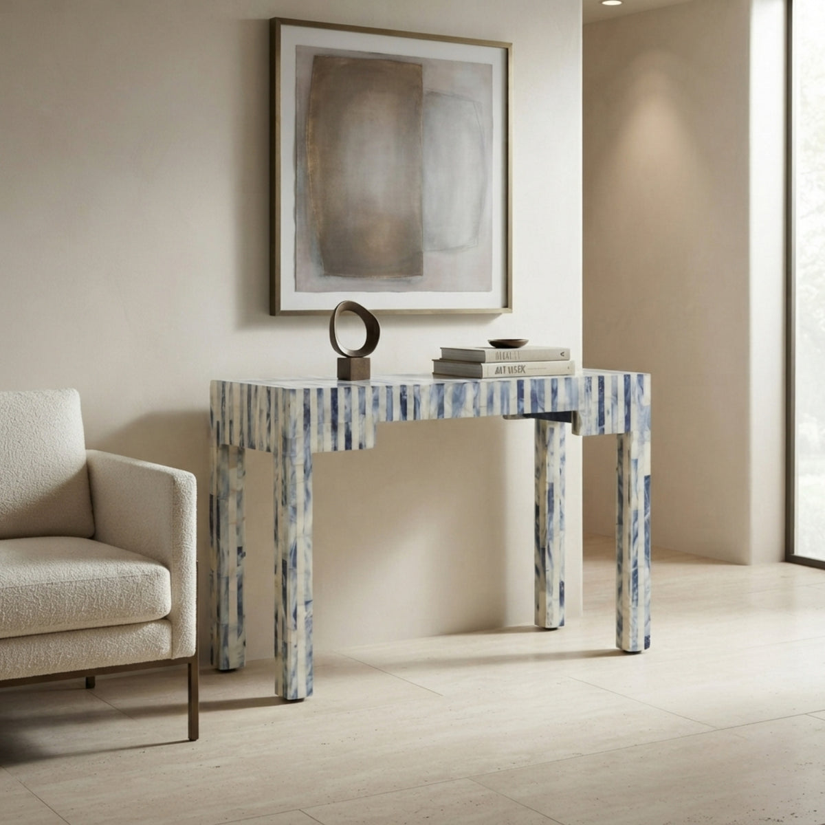 A console table with a blue and white marbled pattern, styled in a modern living room setting next to a beige armchair under a framed abstract painting.