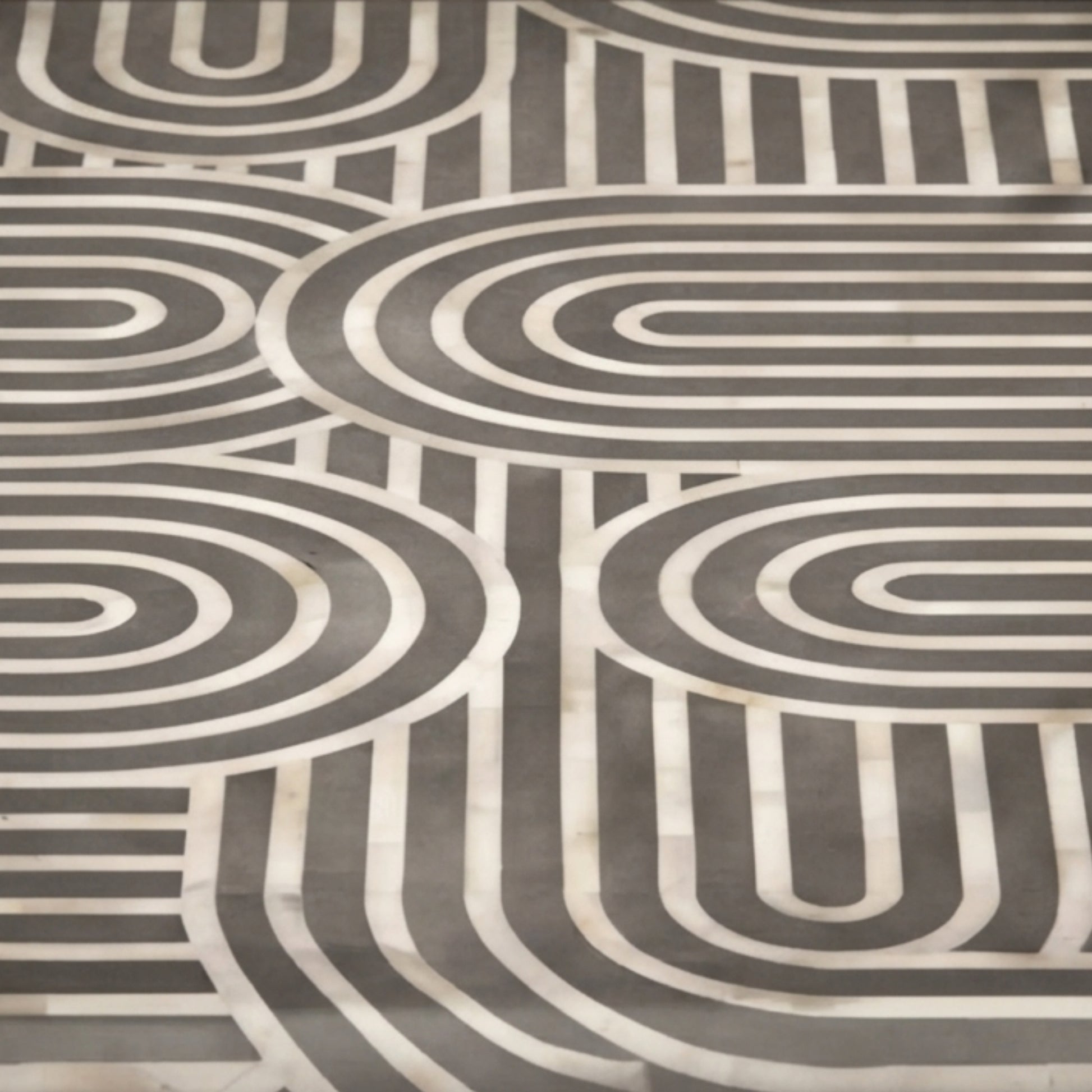 A close-up of a patterned fabric or wallpaper featuring a mid-century modern geometric design with concentric arches and stripes in dark gray and off-white.