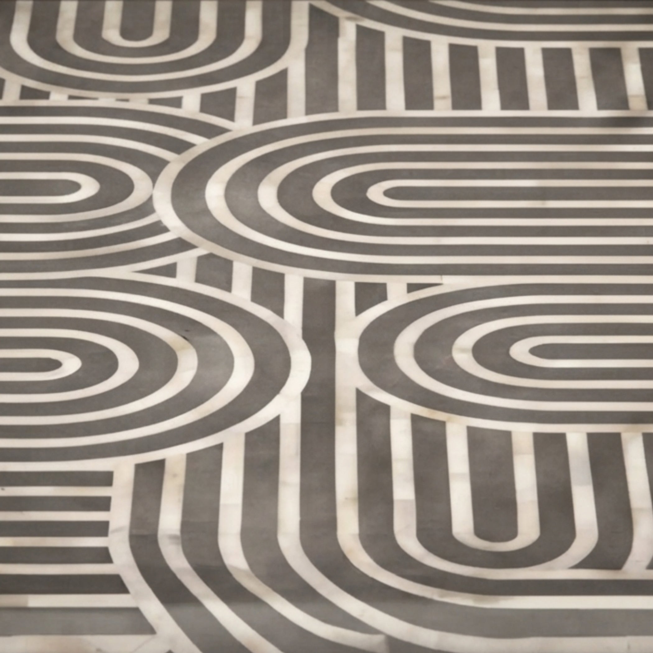 A close-up of a patterned fabric or wallpaper featuring a mid-century modern geometric design with concentric arches and stripes in dark gray and off-white.